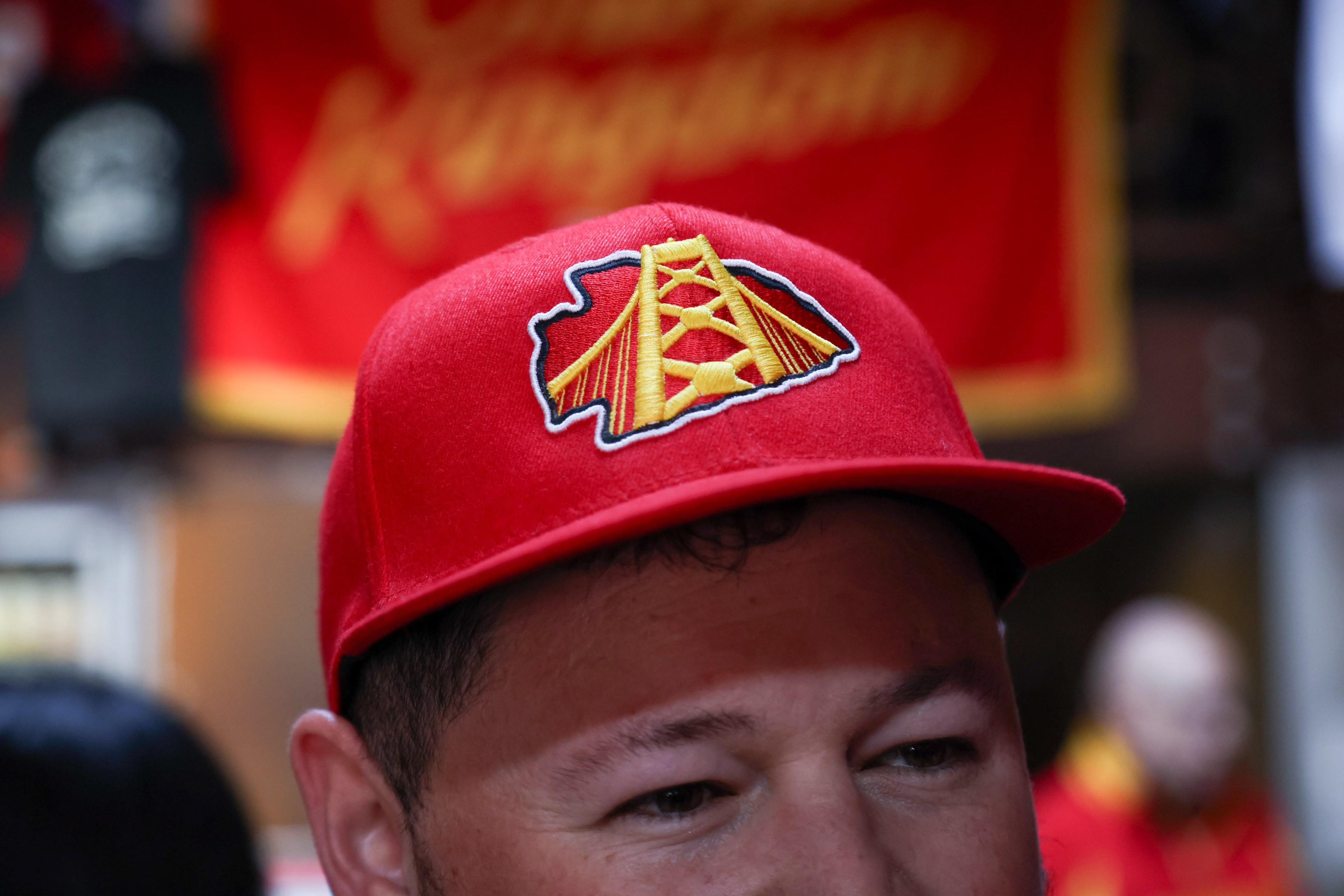 A man shows off red baseball cap with the golden gate bridge in a Kansas City chiefs logo