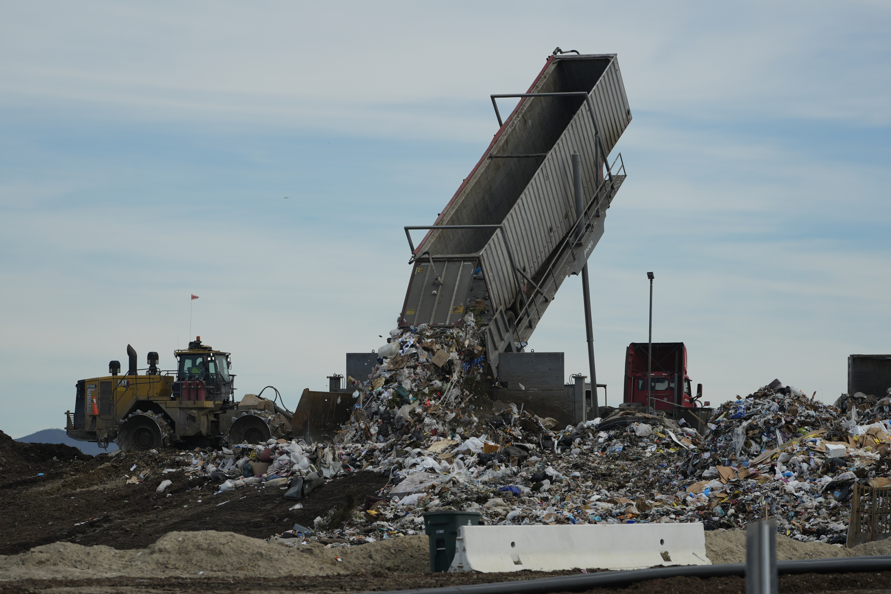 a large trash-unloading machine is seen dumping garbage at a landfill by day