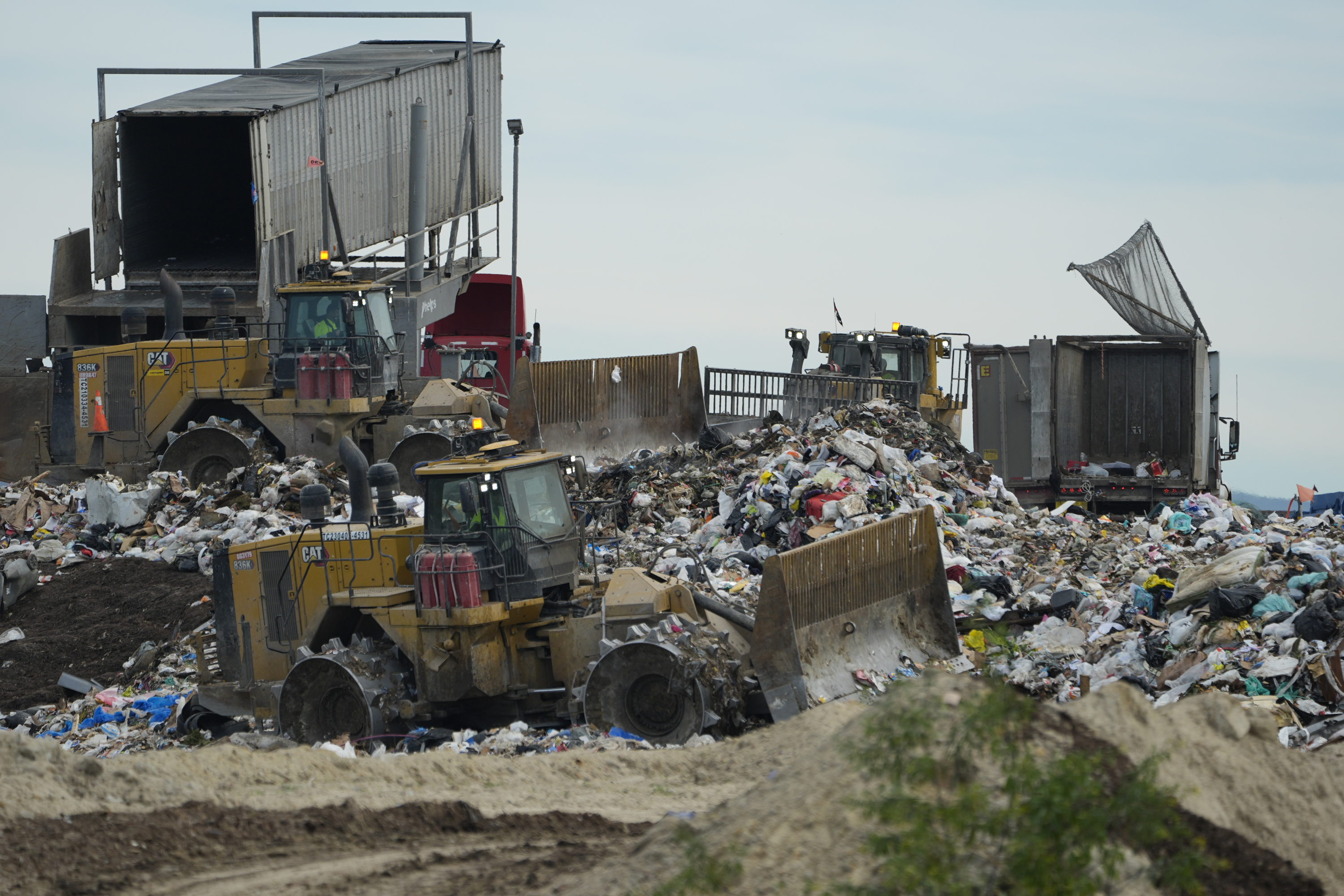a landfill is seen by day, with heavy machinery at work sorting garbage