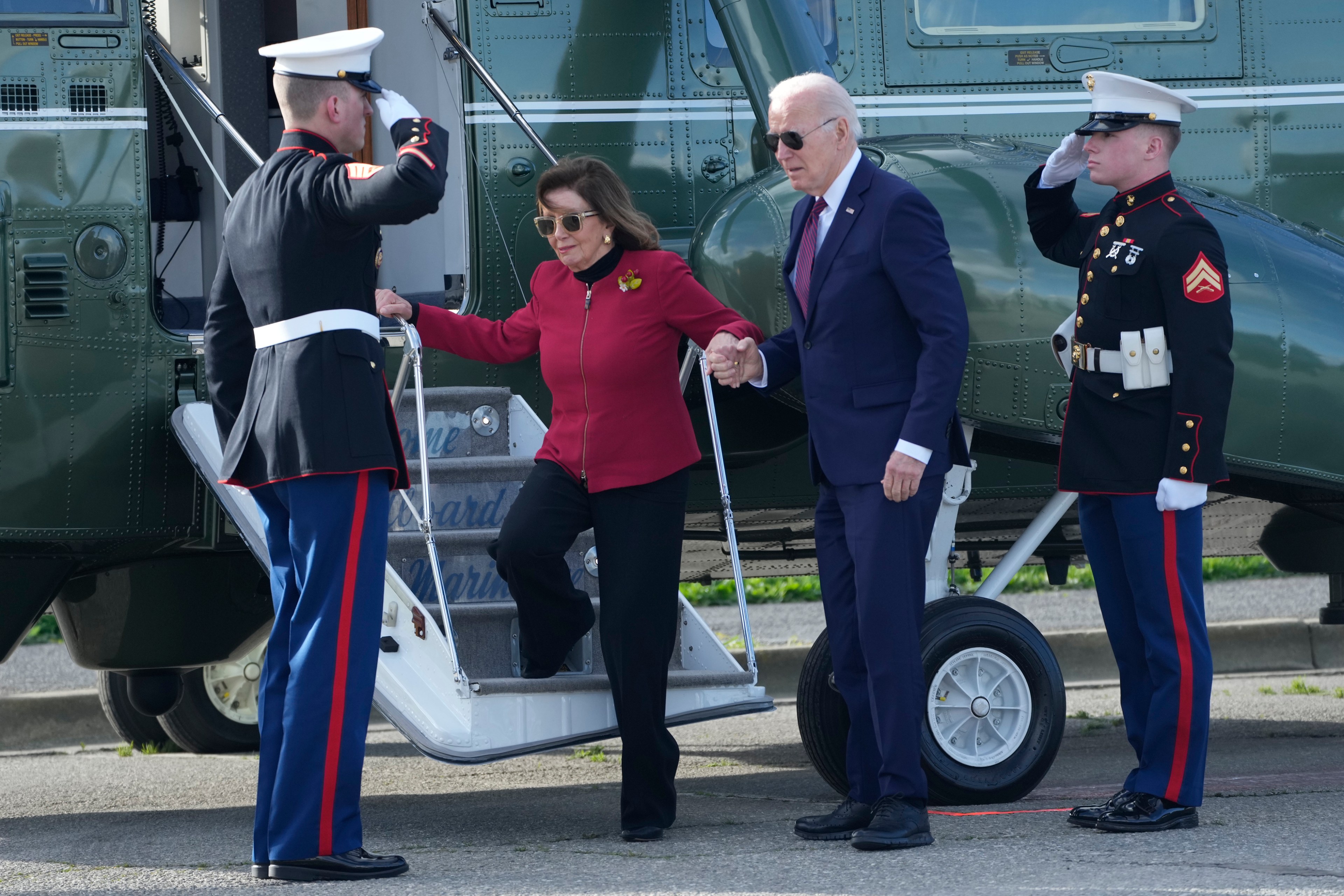 Nancy Pelosi steps off a helicopter with the help of President Joe Biden as two marines salute on either side.