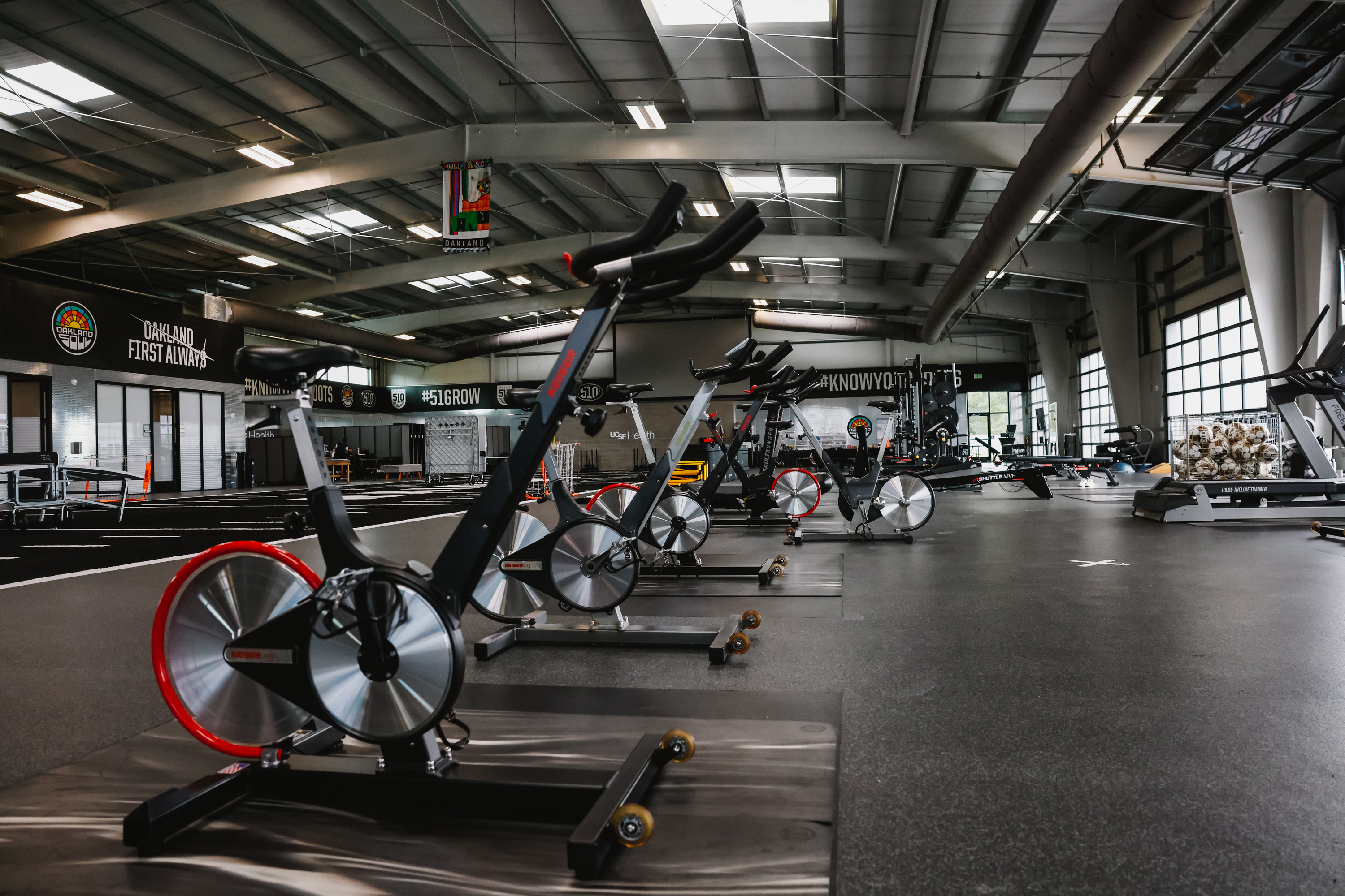A spacious, modern gym with various exercise equipment, weight racks, and motivational slogans on walls.