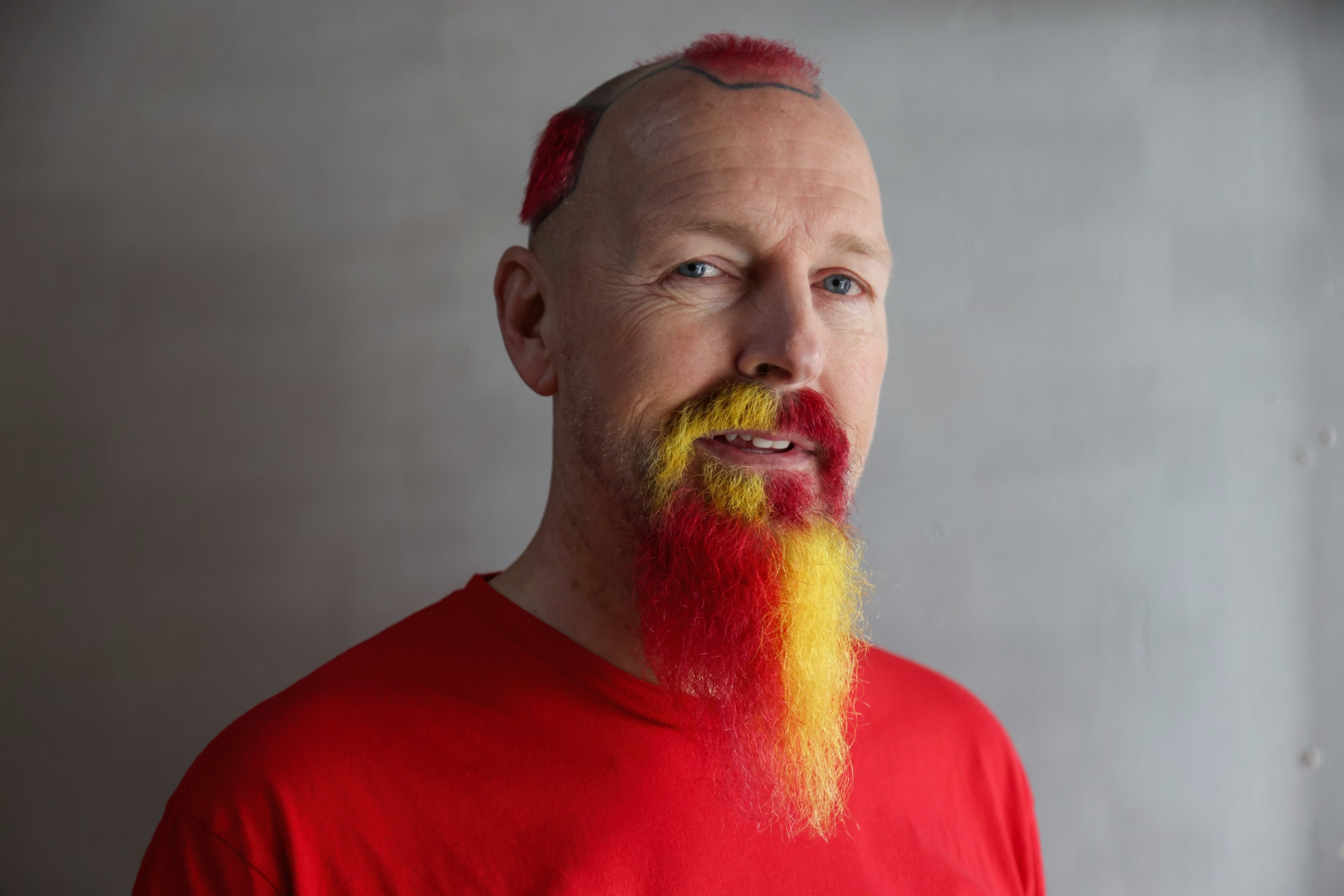 Man wearing red shirt with yellow and red dyed facial hair