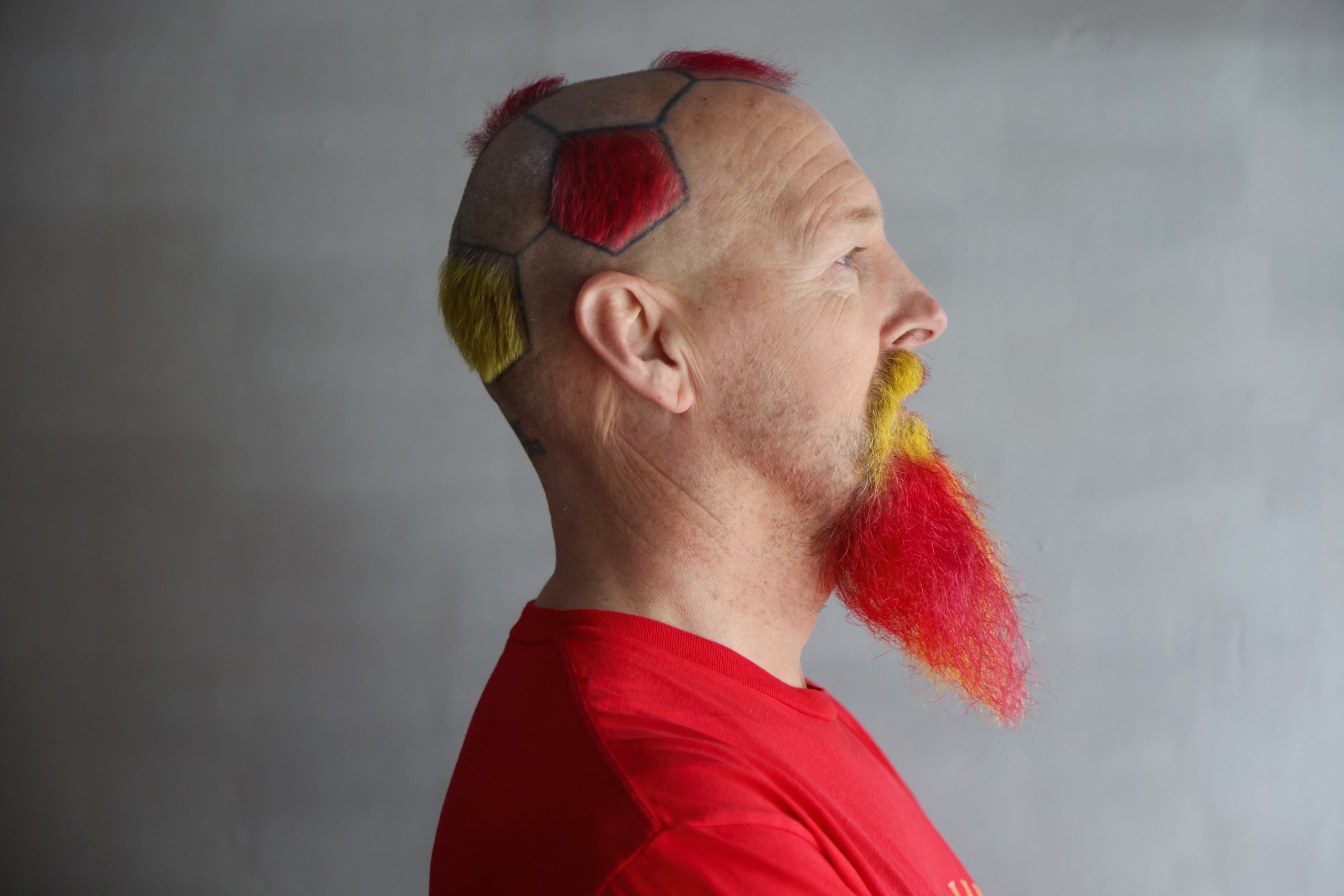 A man with a soccer ball pattern shaved and dyed into his hair and beard, showcasing red, yellow, and natural colors.