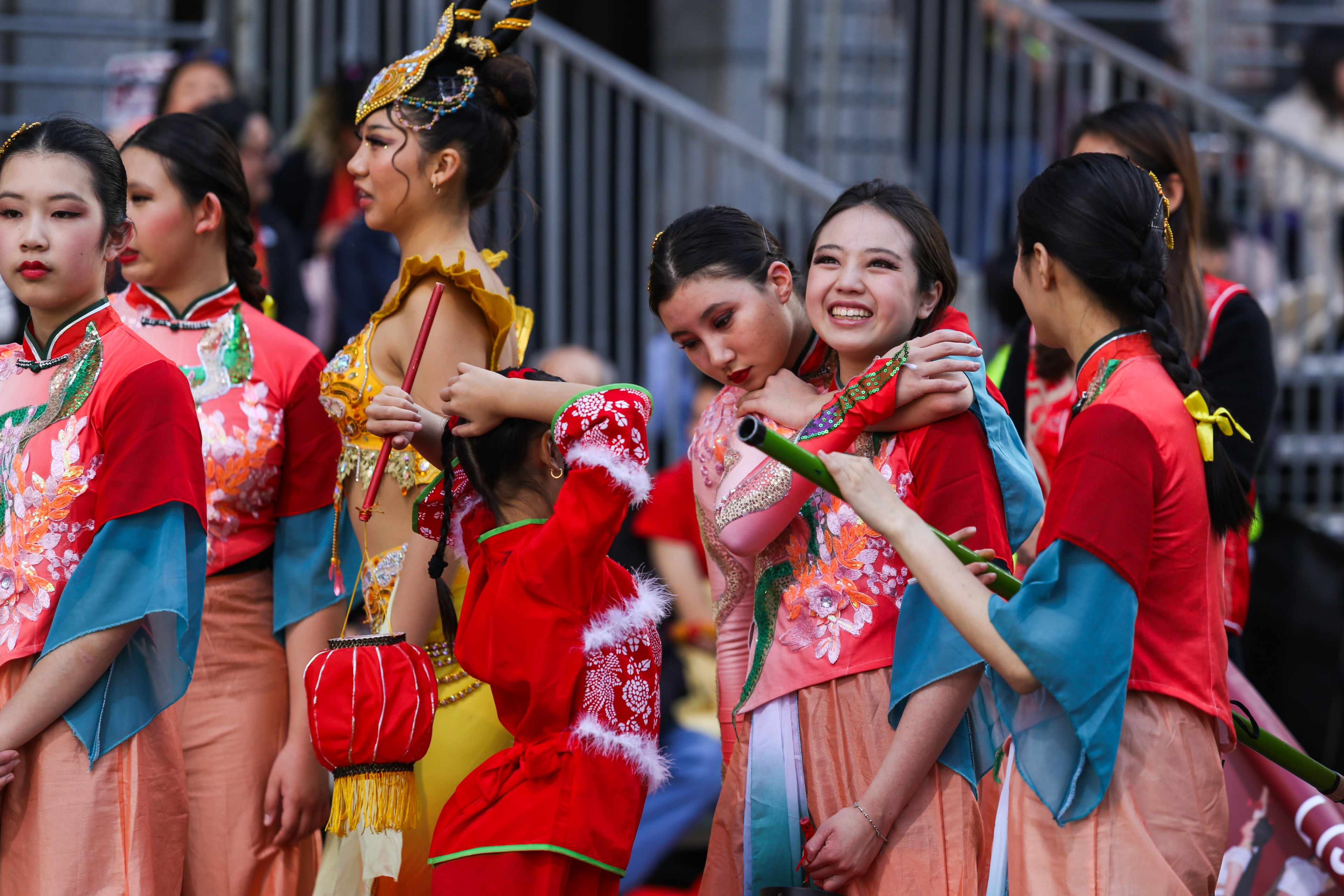 Group of people in colorful traditional Asian attire, smiling and interacting with each other, some holding props.