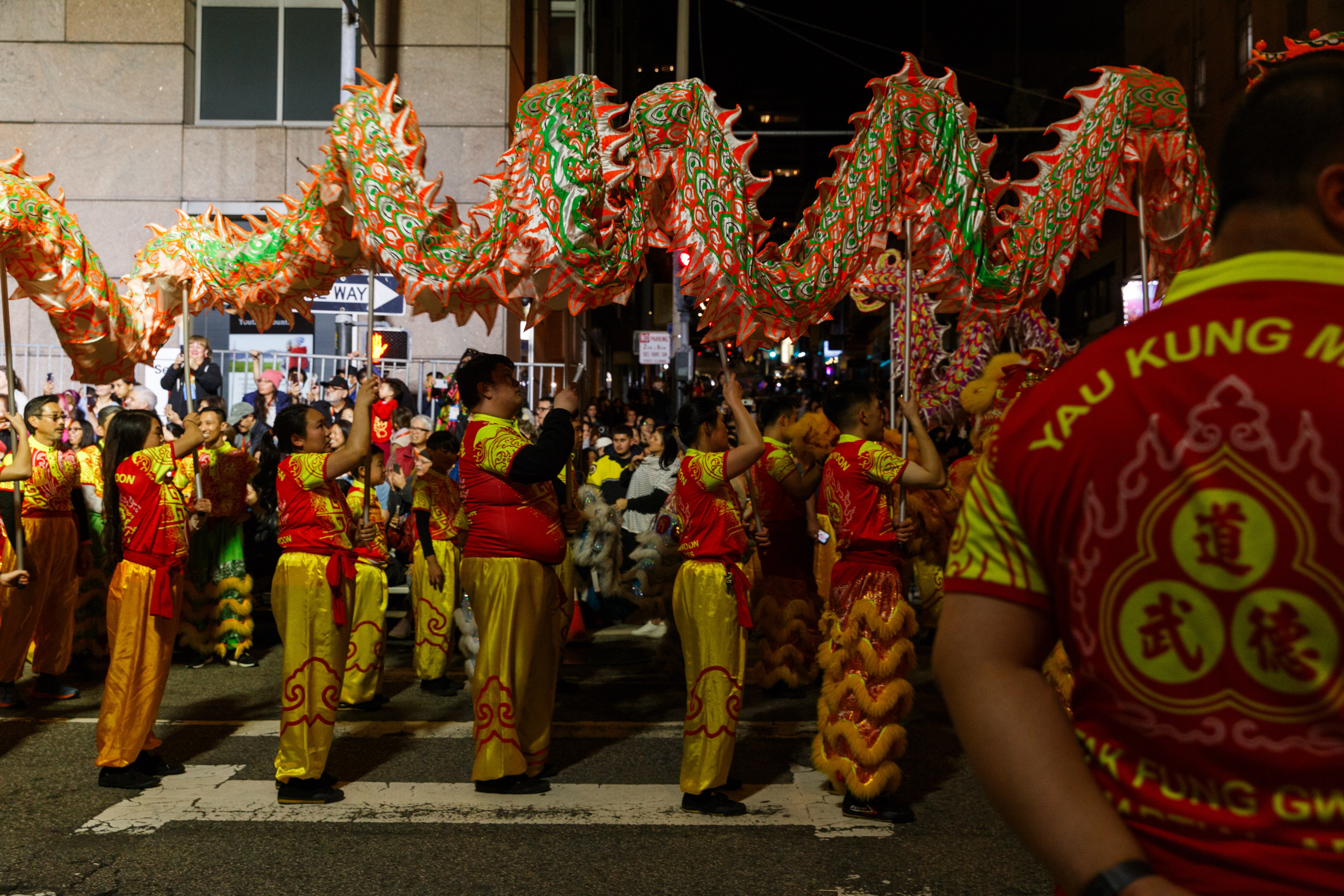 Performers in traditional attire carry a fiery red and green dragon in a vibrant night street parade.