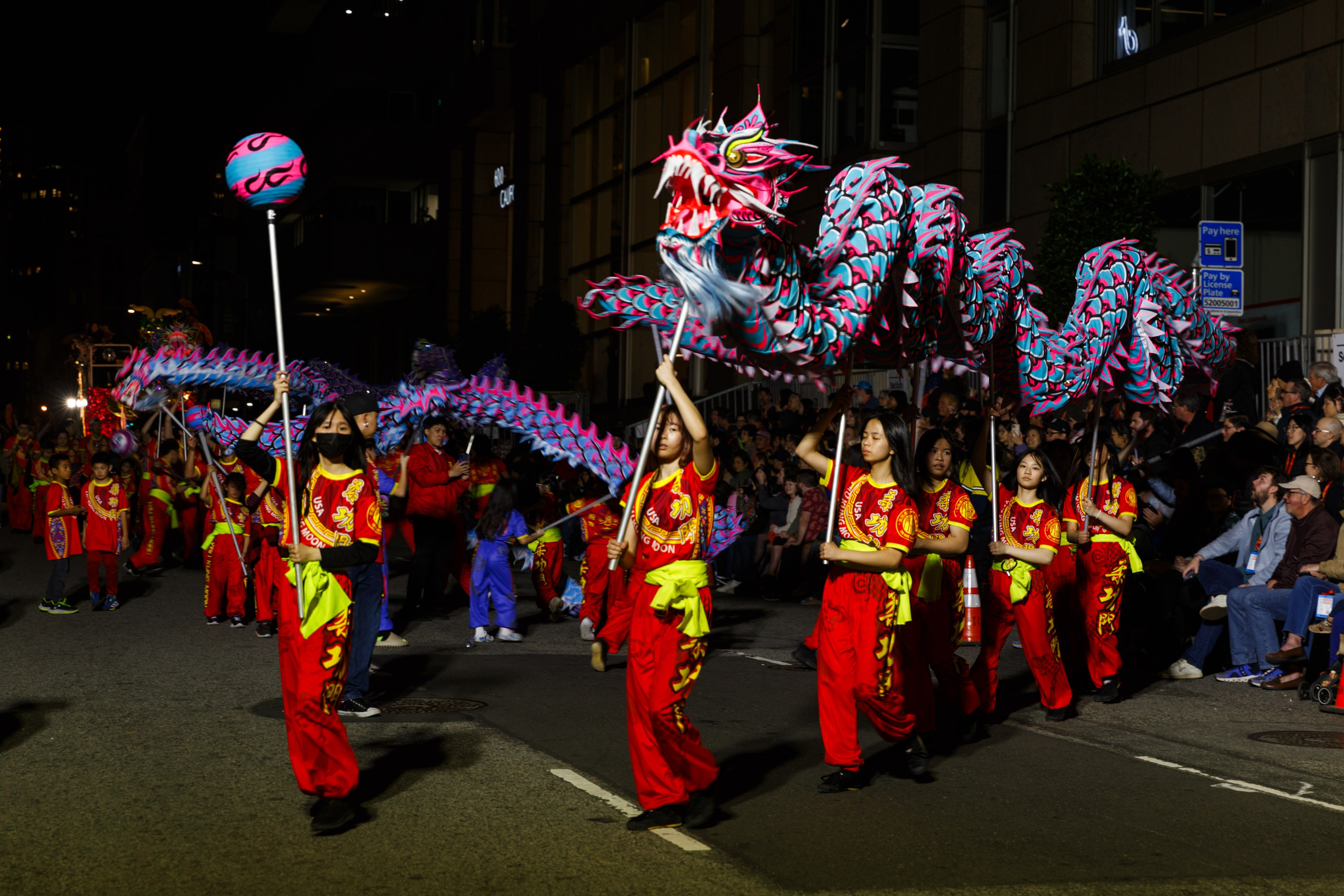 A vibrant dragon dance at night with performers in red and spectators watching.
