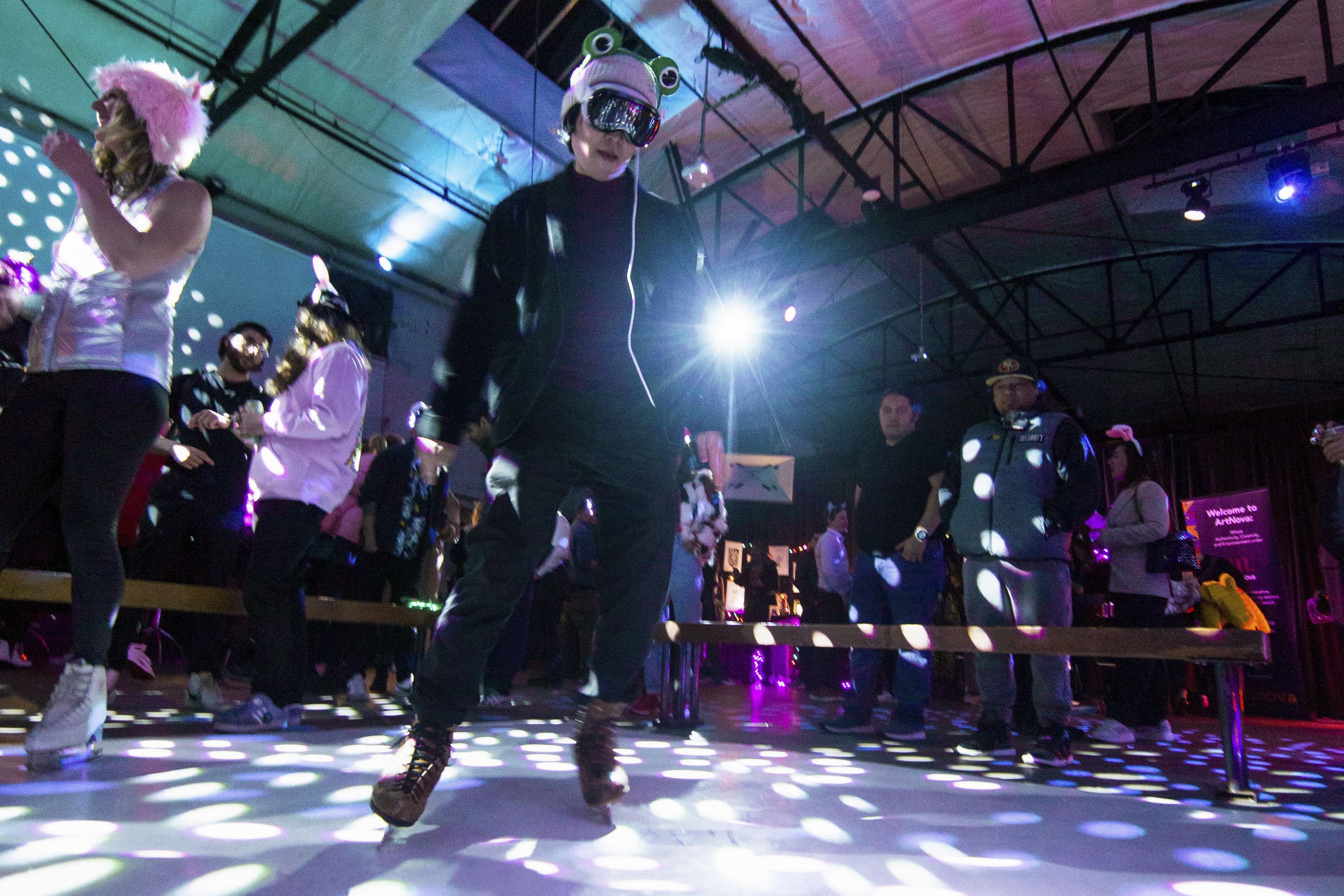 People skate in a dimly lit venue with colorful lights and disco vibes.