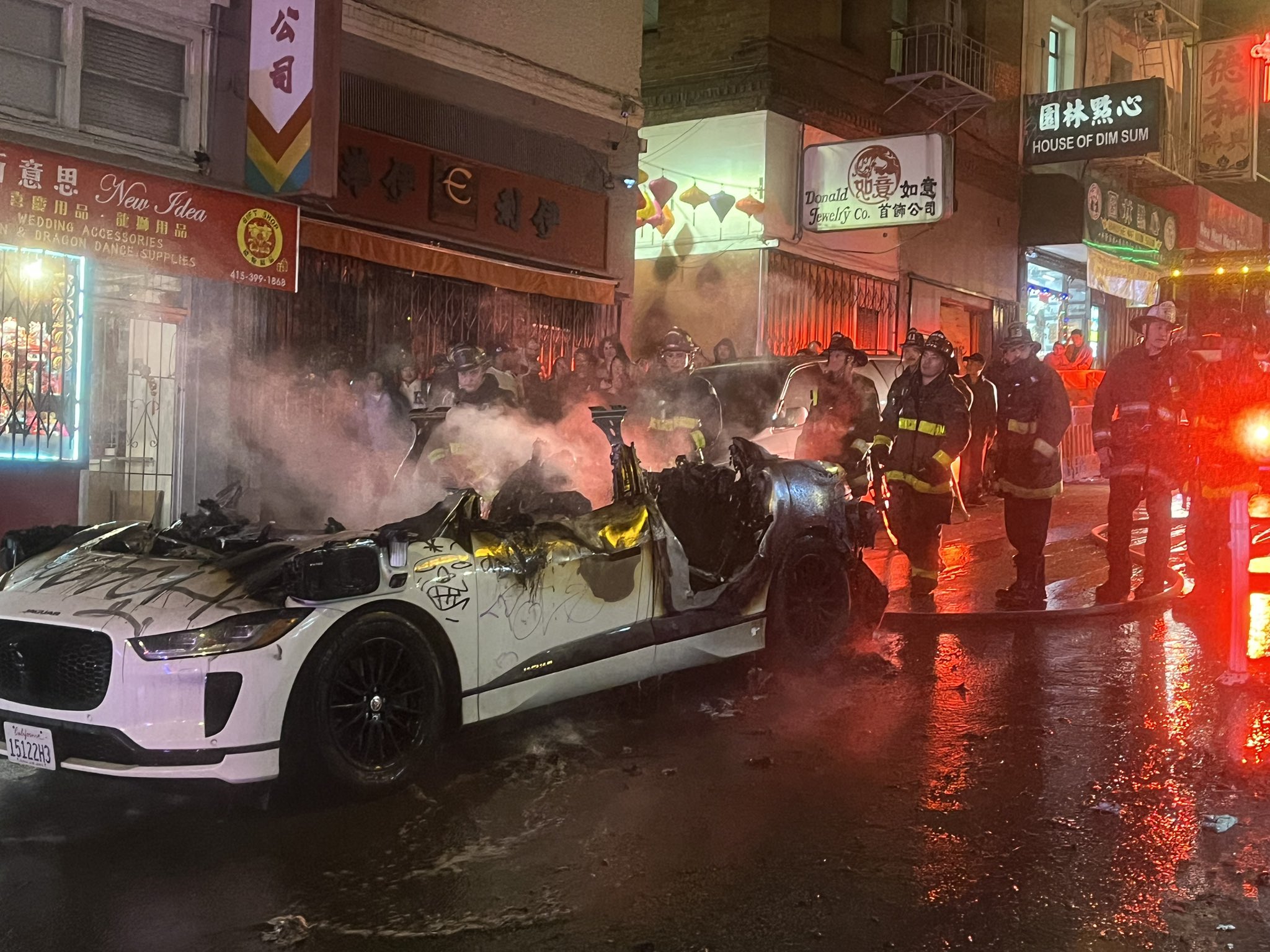 A smoking car hulk beside fire fighters.