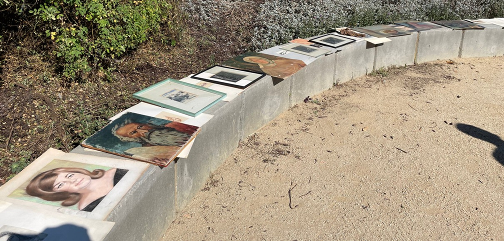 A series of framed paintings and pictures laid out along an outdoor curved wall.