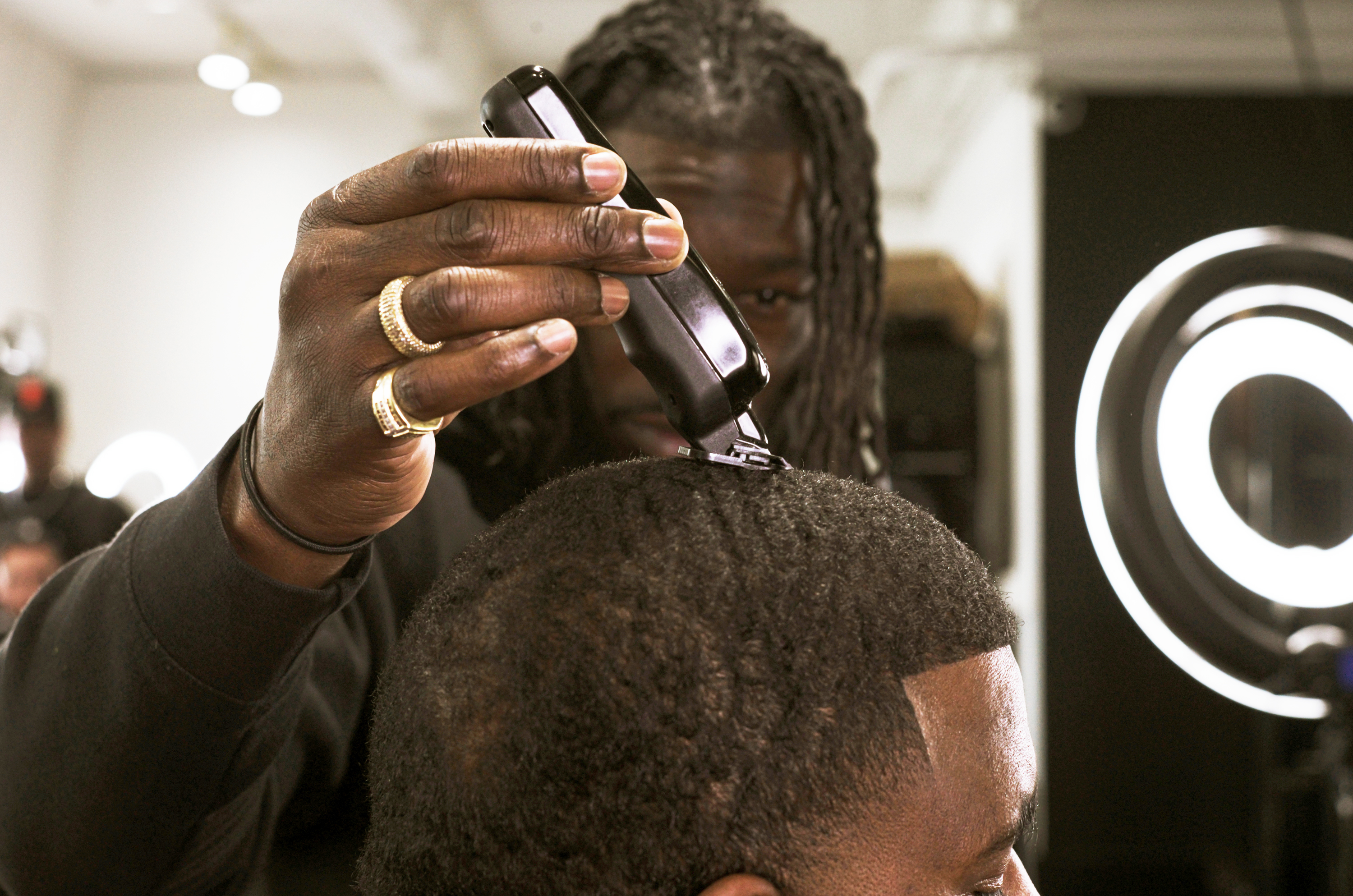 A barber with braided hair trims a client's hair with clippers in a salon.