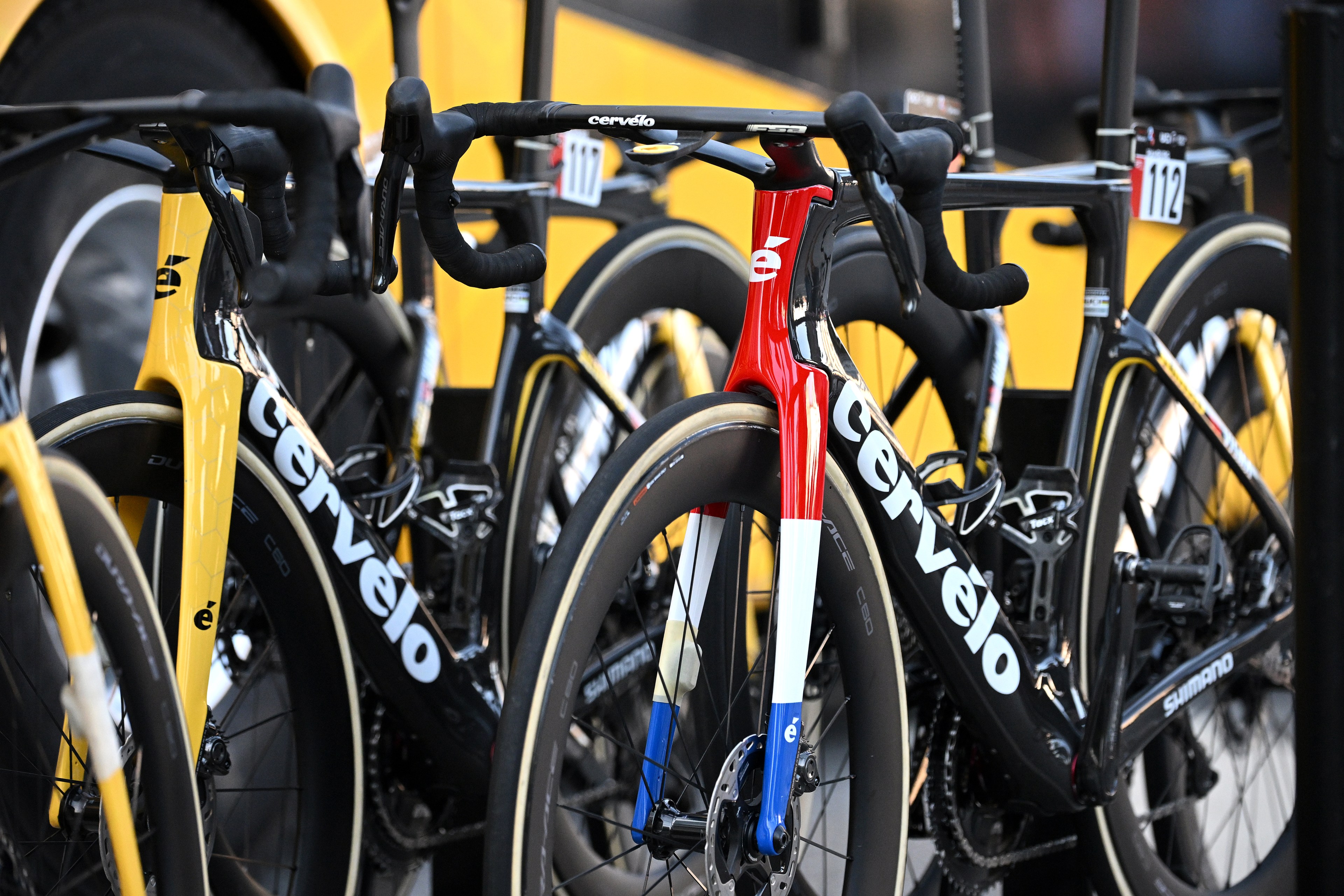 A lineup of yellow and one red-and-white Cervélo road bikes with Shimano parts, mounted on a vehicle rack.