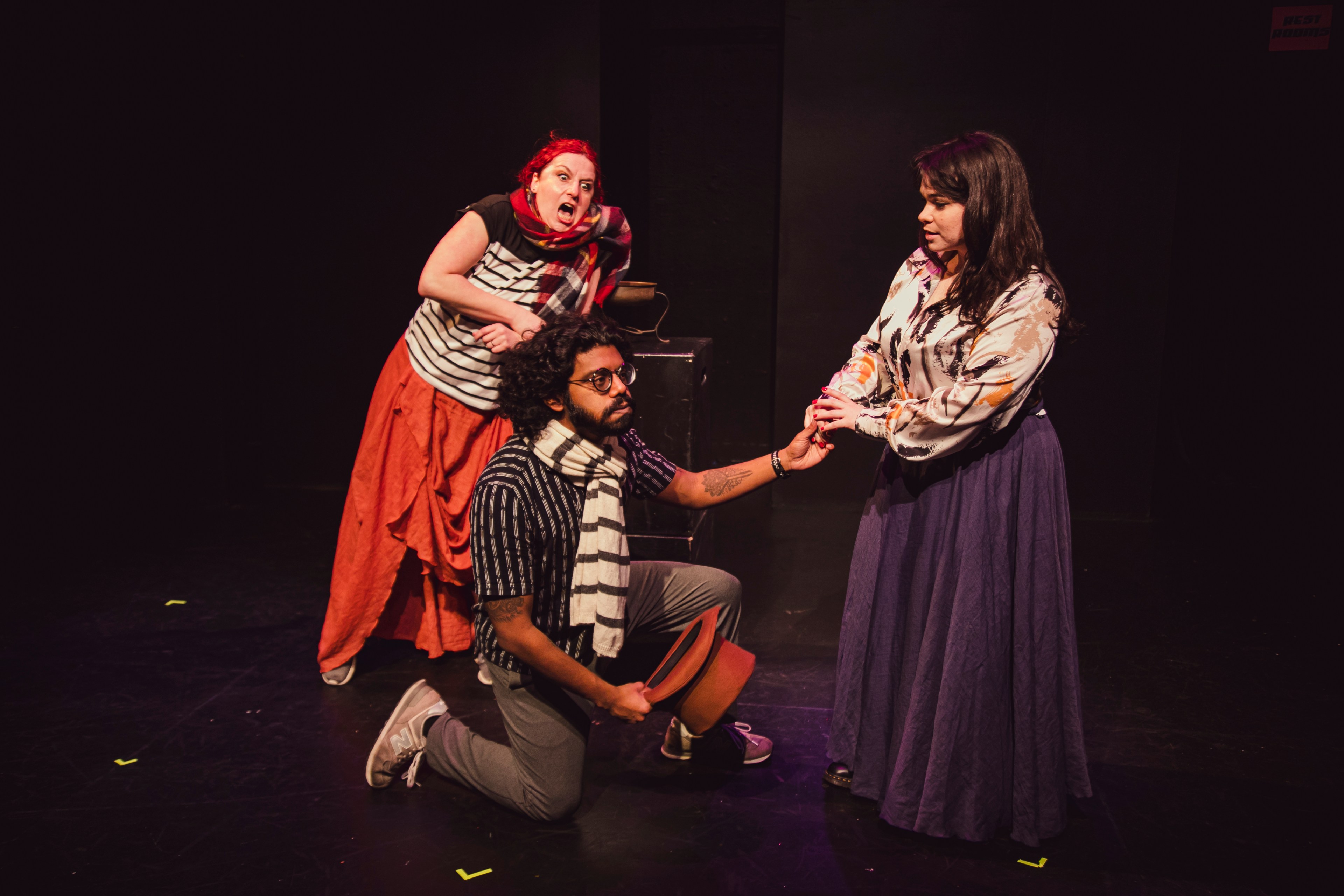 A man kneels down to propose to a woman in a purple skirt while another woman looks in comedy sketch by the San Francisco performance troupe Killing My Lobster.