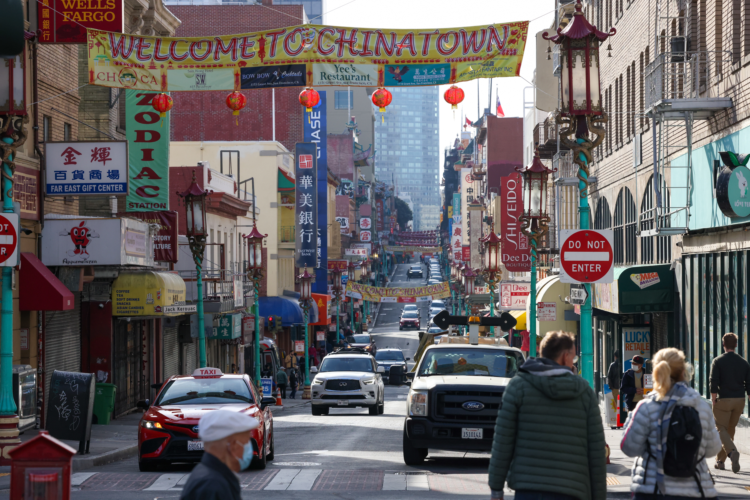 A bustling Chinatown street with a "Welcome" arch, adorned with lanterns, shops, pedestrians, and vehicles.