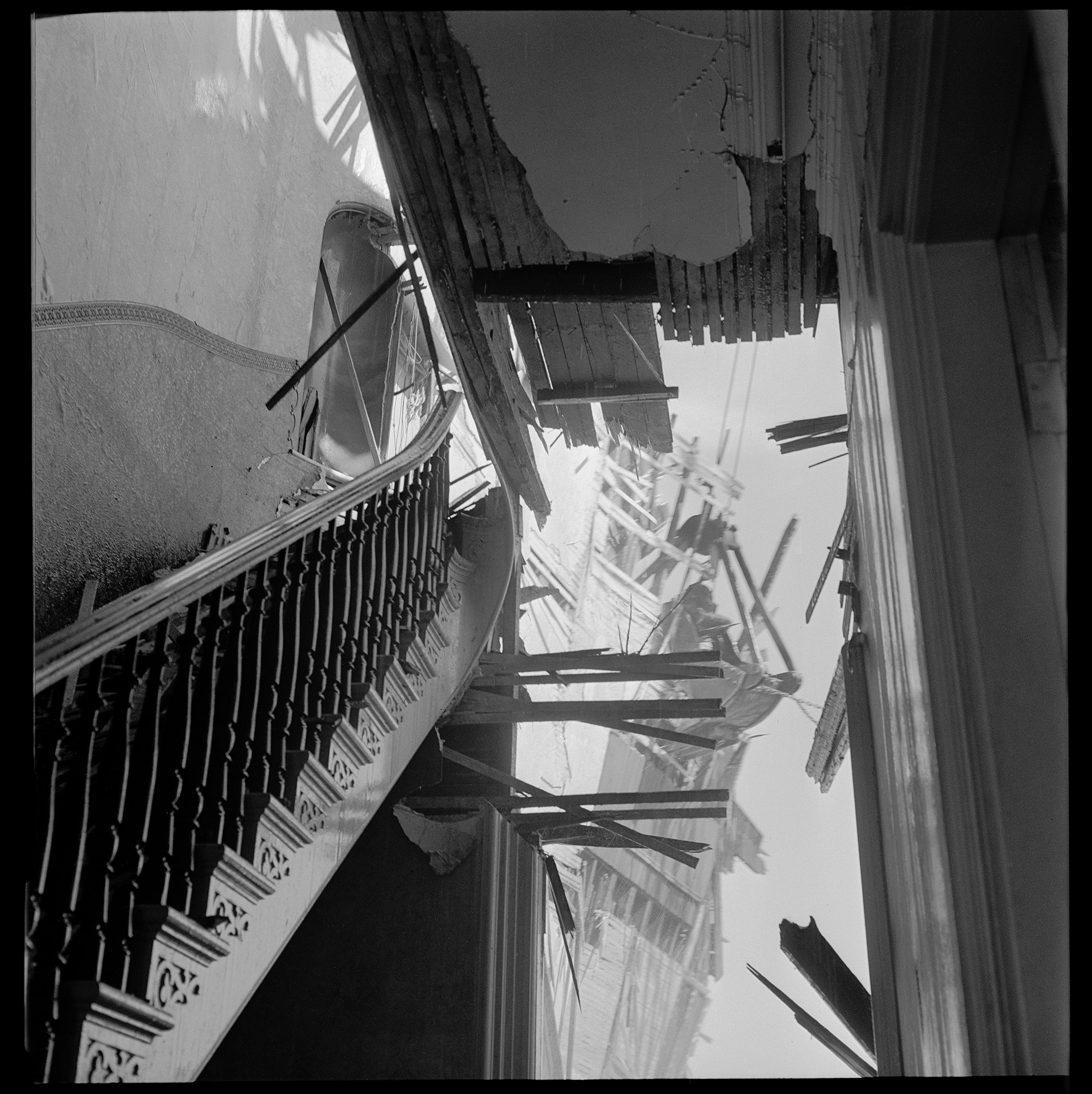 An angled view of a damaged staircase and building debris against a clear sky.