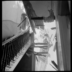 An angled view of a damaged staircase and building debris against a clear sky.