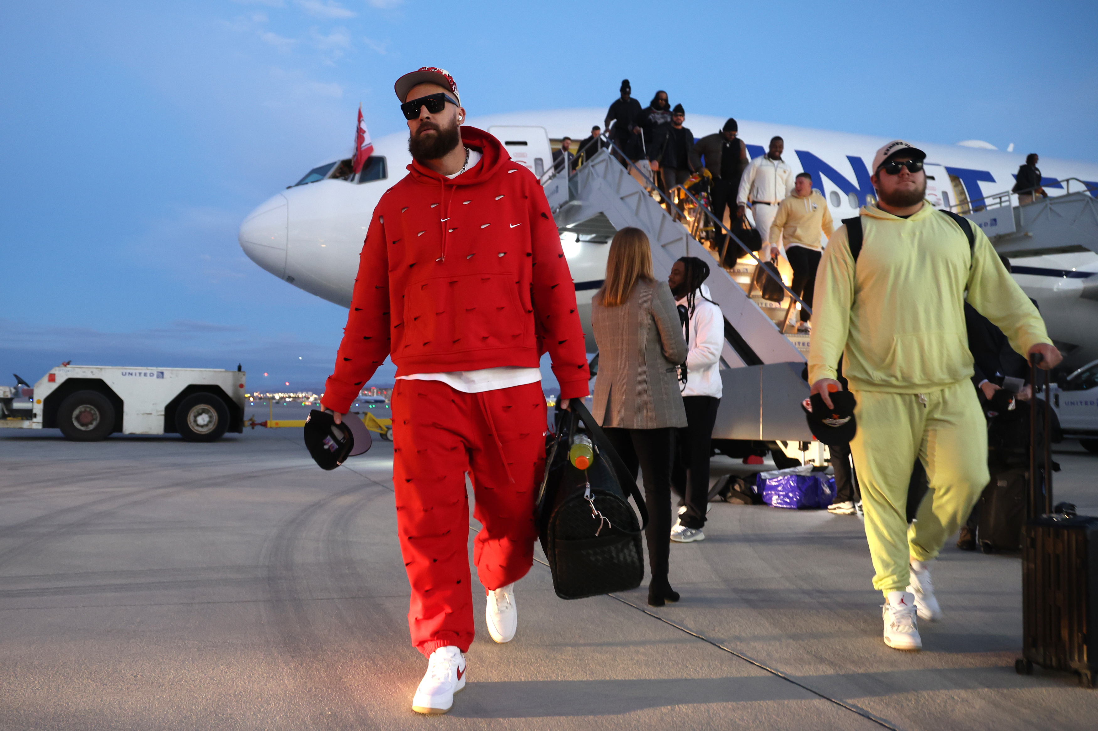 man in a red track suit walks off a plane with a lot of other people following behind