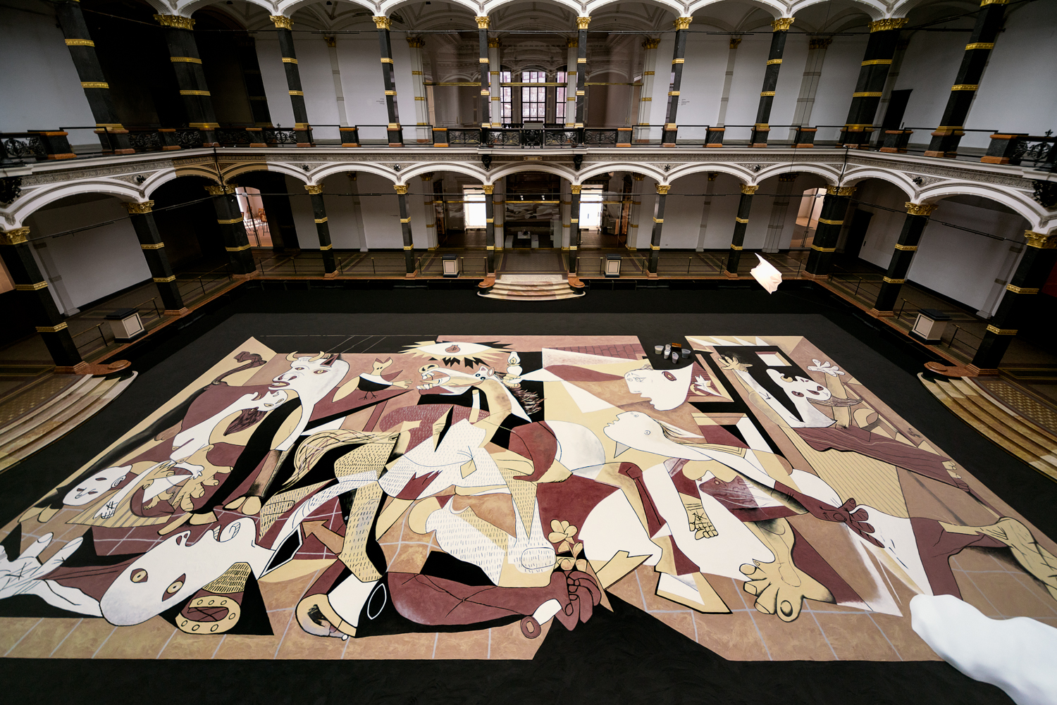 A large, stylized art piece laid out on a grand hall floor with arches and columns.