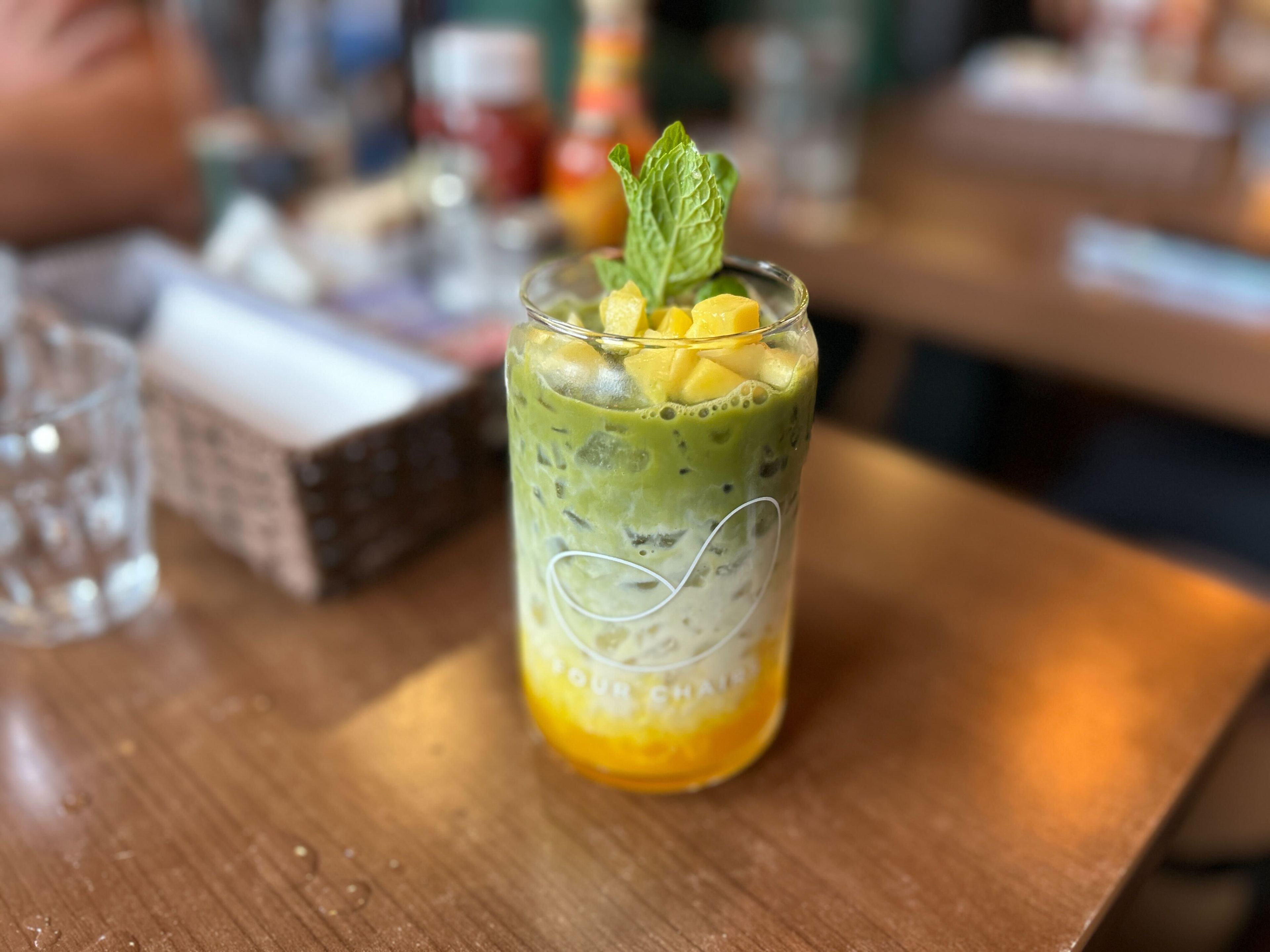 a matcha green tea mango drink in a mason jar-type glass over ice, topped with mango pieces