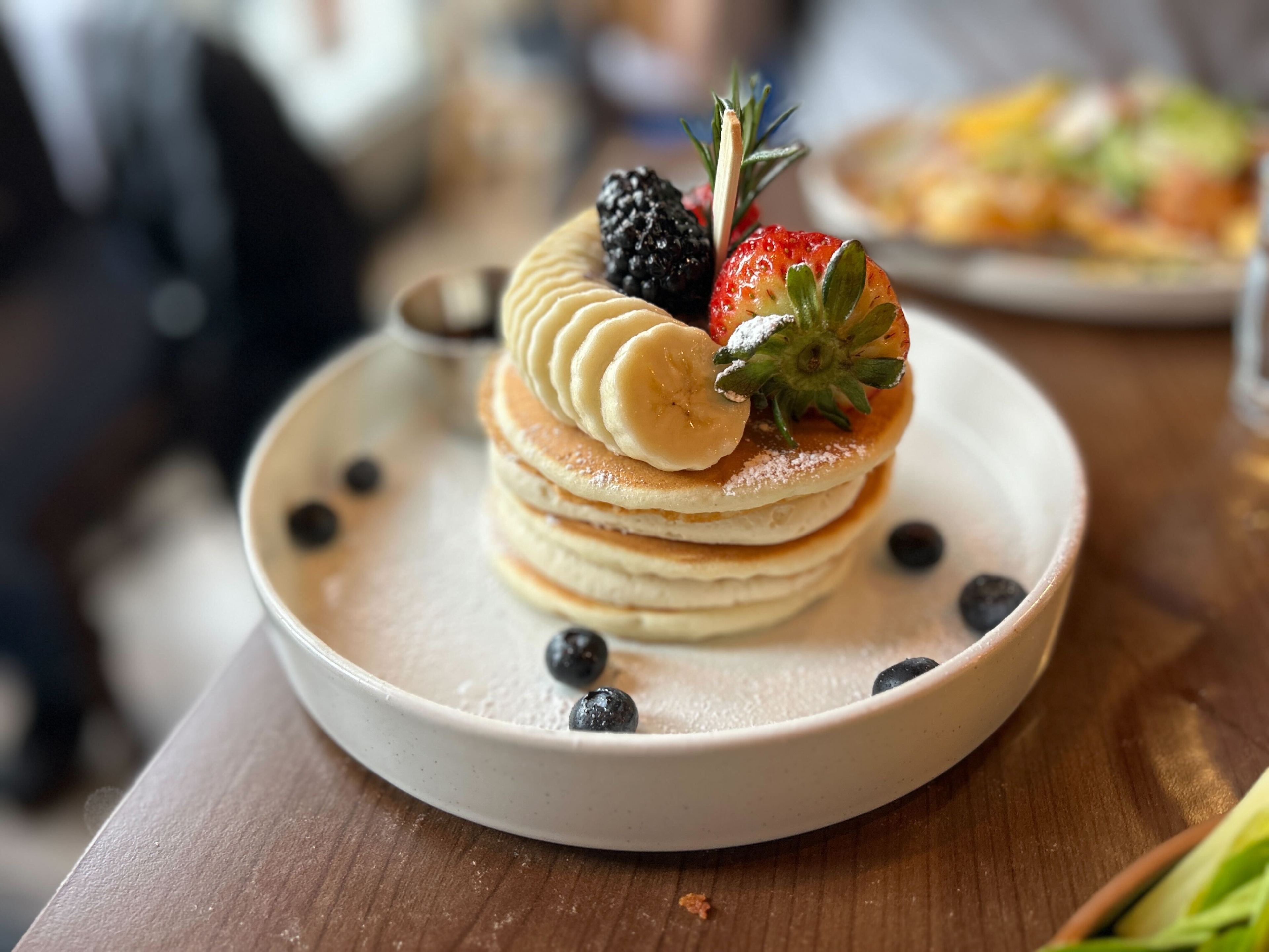 a stack of mascarpone pancakes topped with bananas and fruit and sprinkled with blueberries in a white dish