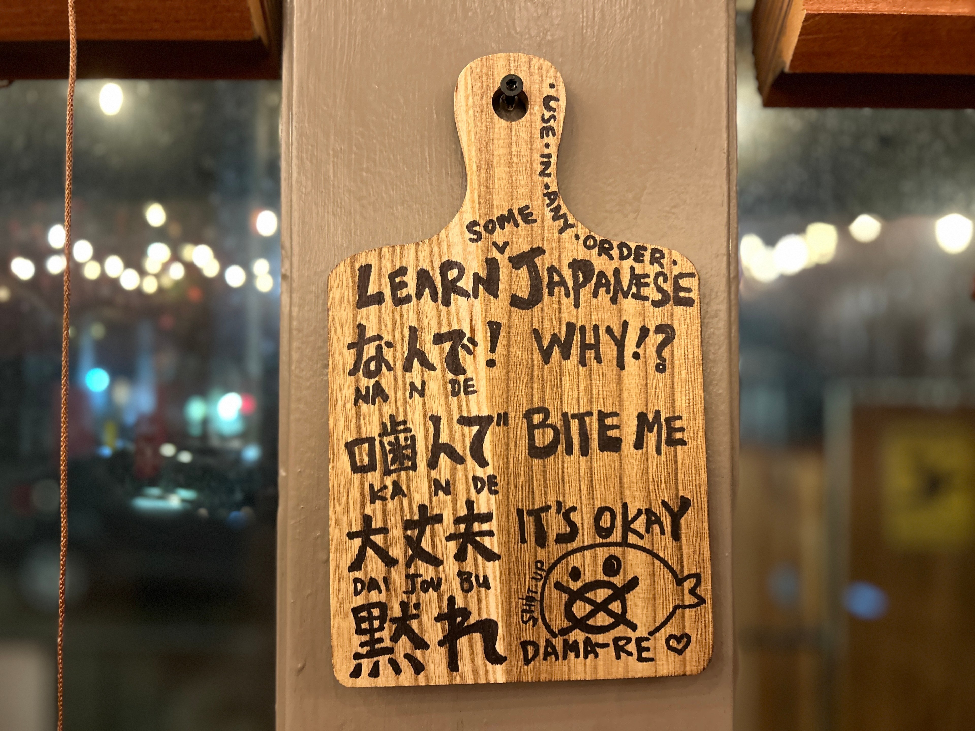 a wall-mounted paddle with translations of tongue-in-cheek Japanese phrases