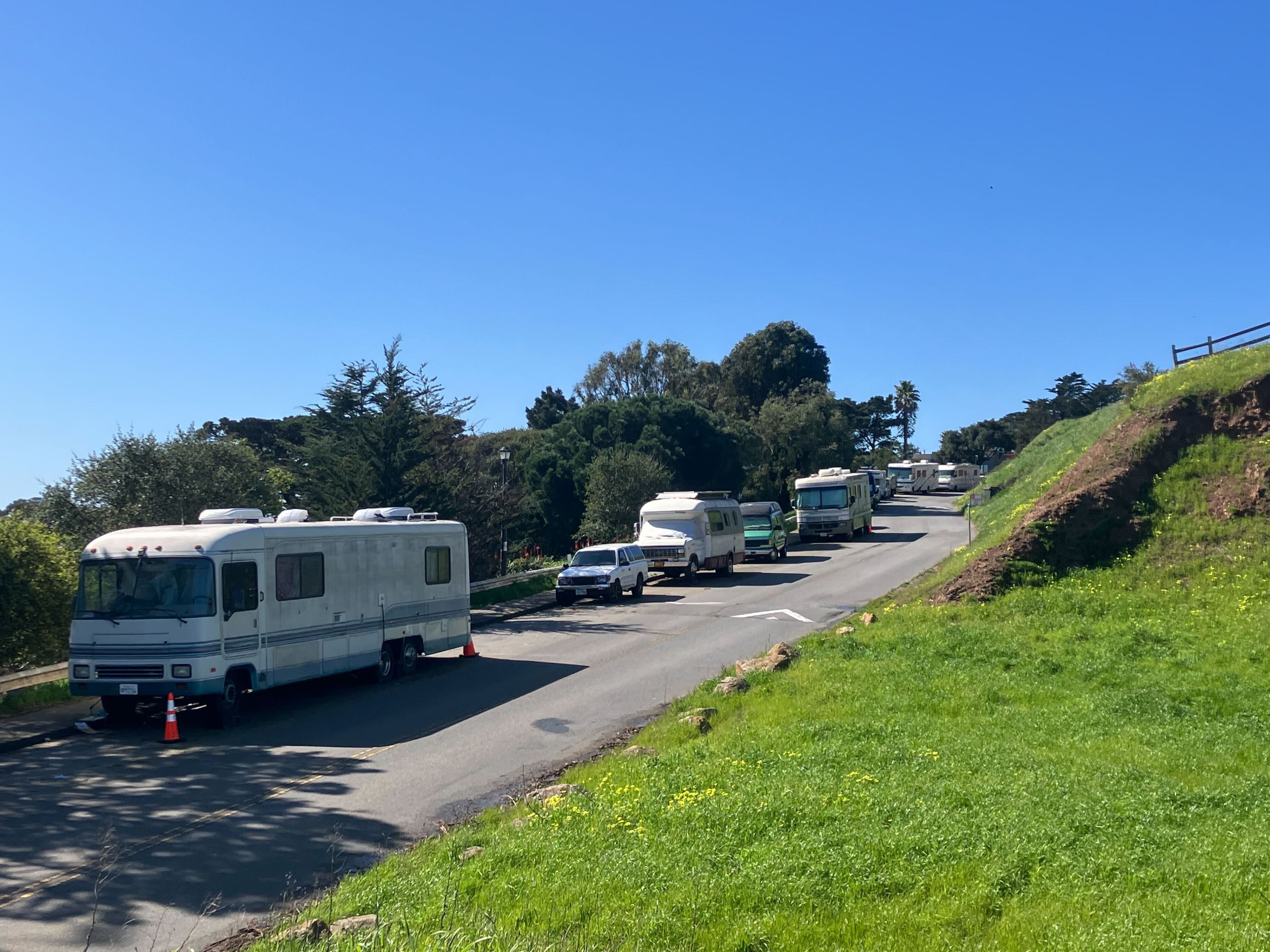 Several RVs parked along a roadside with grass and trees under a clear blue sky.
