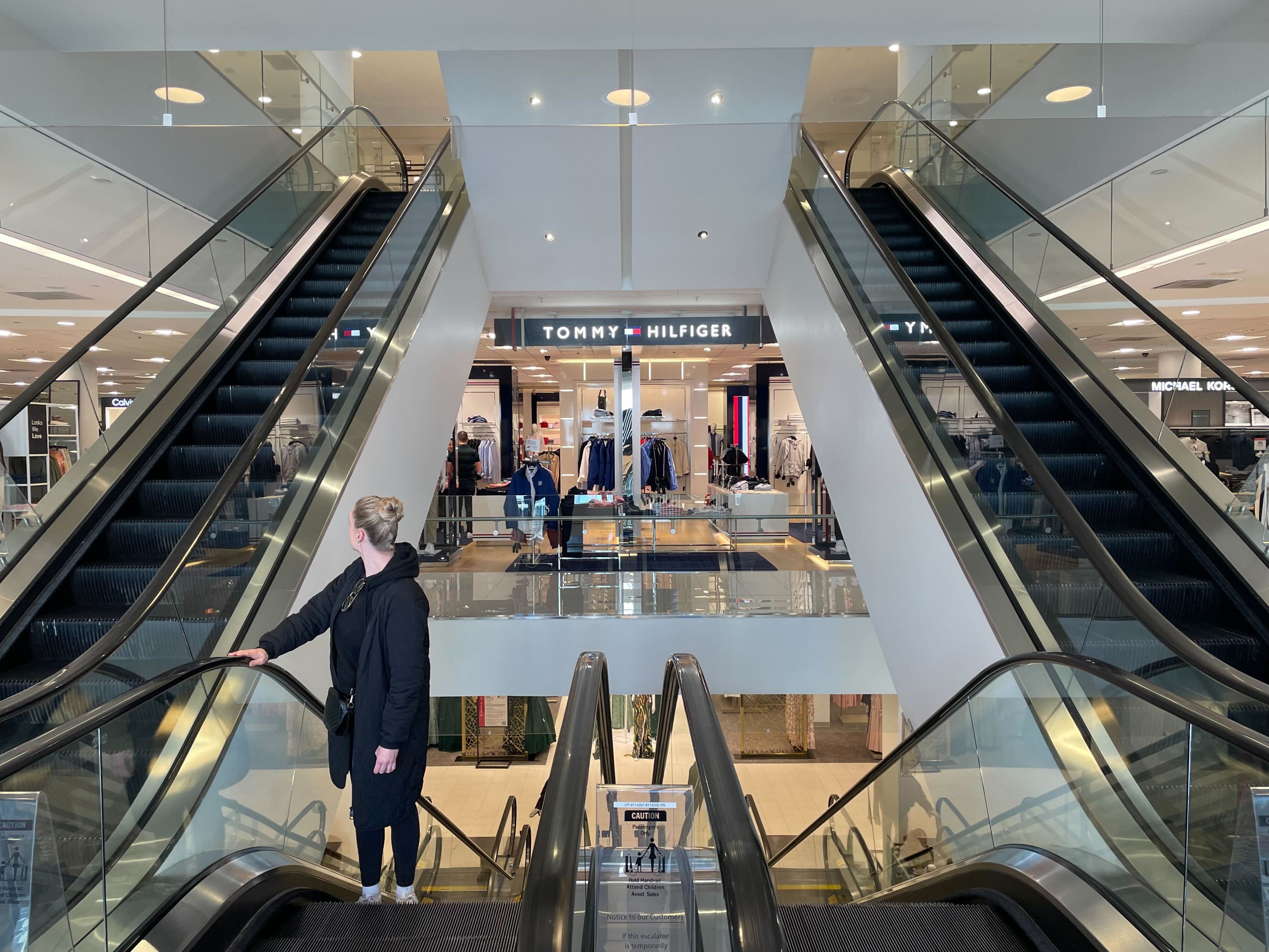 A person riding an escalator inside a department store looks behind her.