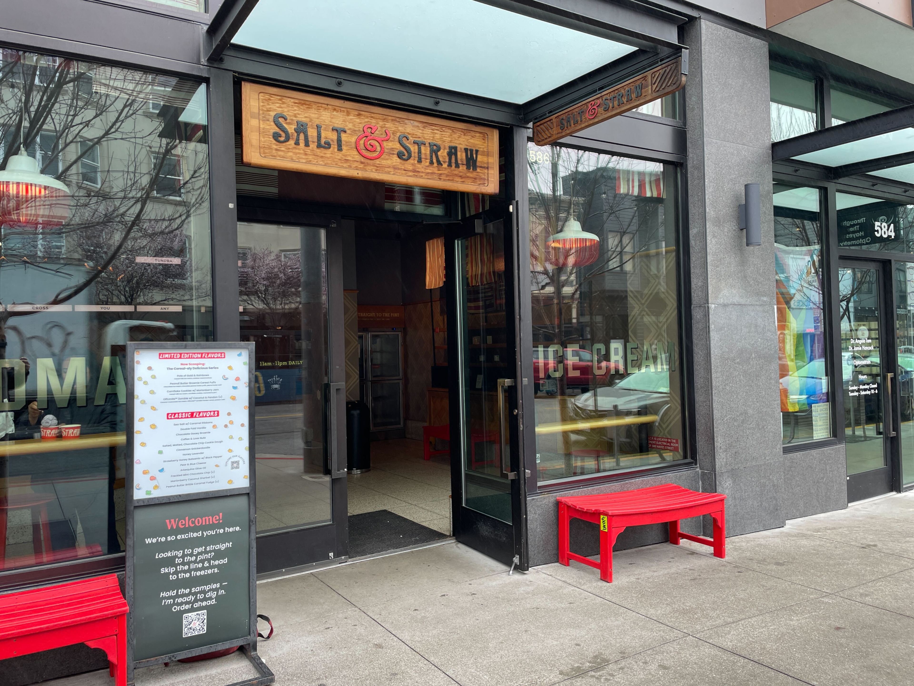 An ice cream shop entrance with a red bench outside and a menu board displaying flavors.