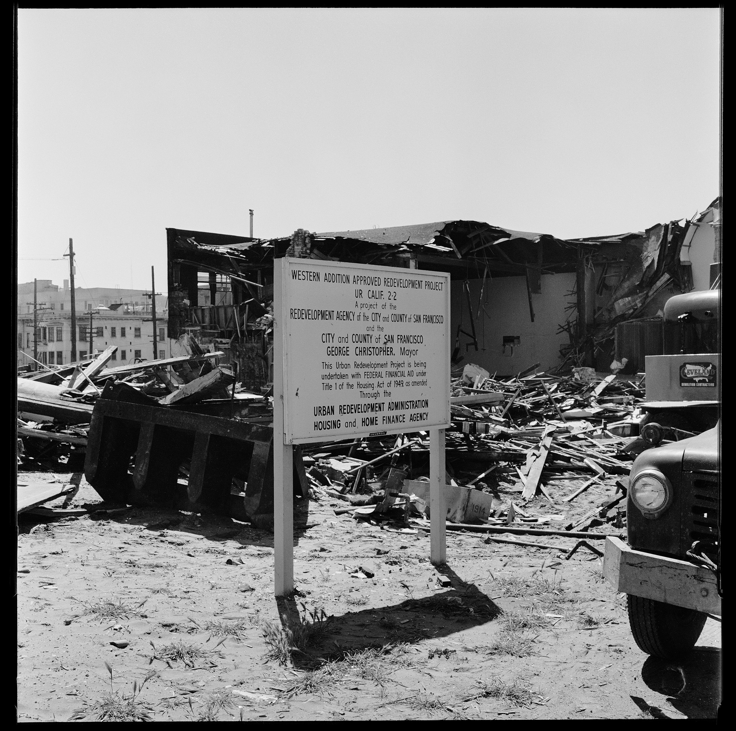 A black and white photo shows a demolished building with a sign about redevelopment.