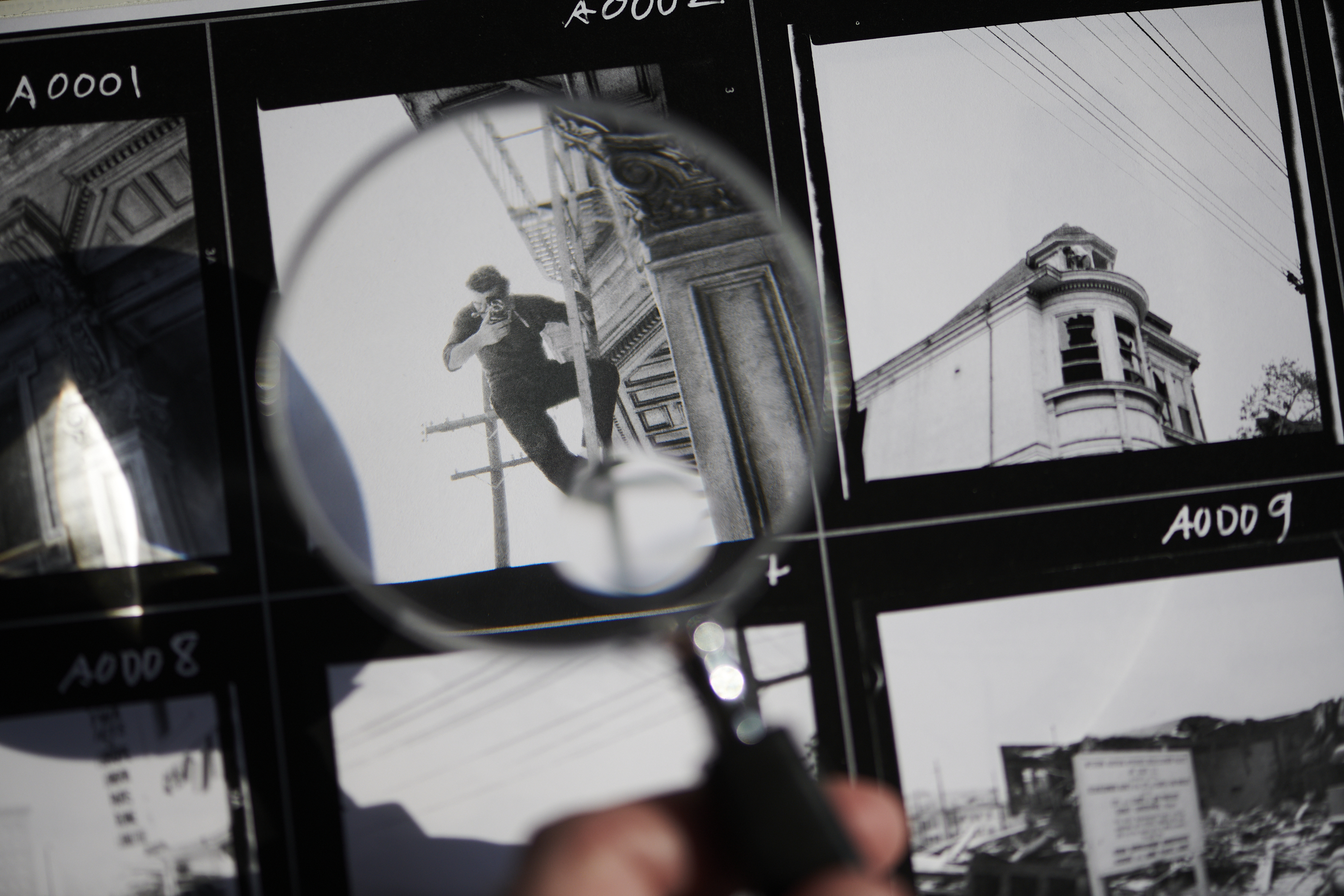A magnifying glass focuses on a film strip image of a person climbing a pole, surrounded by other black-and-white photos.