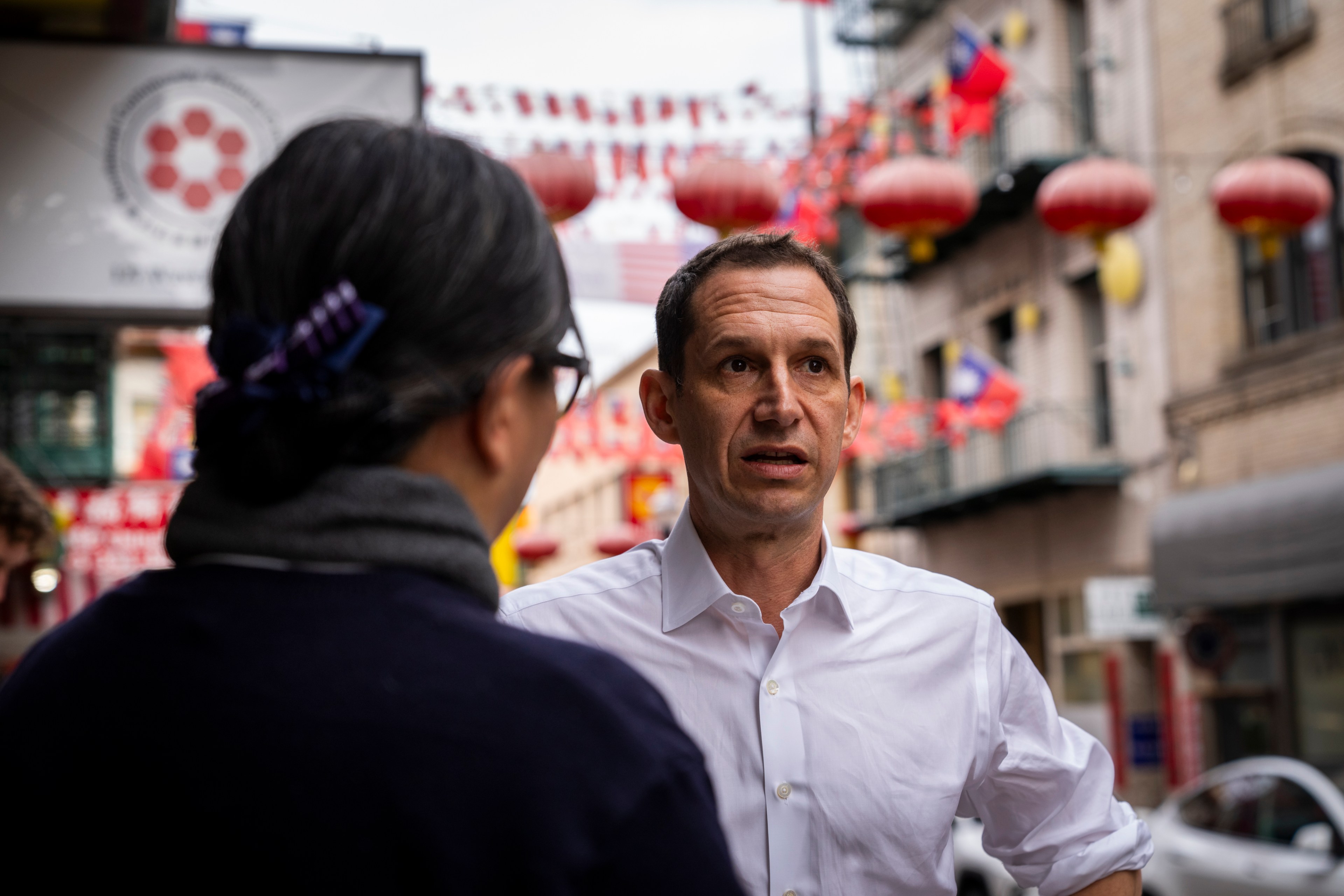 A man converses with someone in a street lined with red lanterns and festive flags.