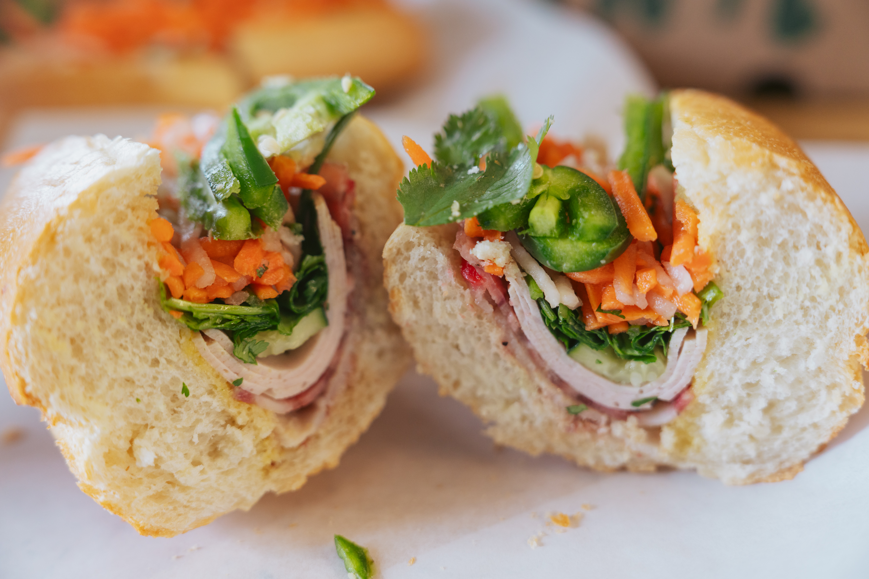 a banh mi sandwich made with turkey, carrots, cilantro and jalapenos on a roll, cut in half