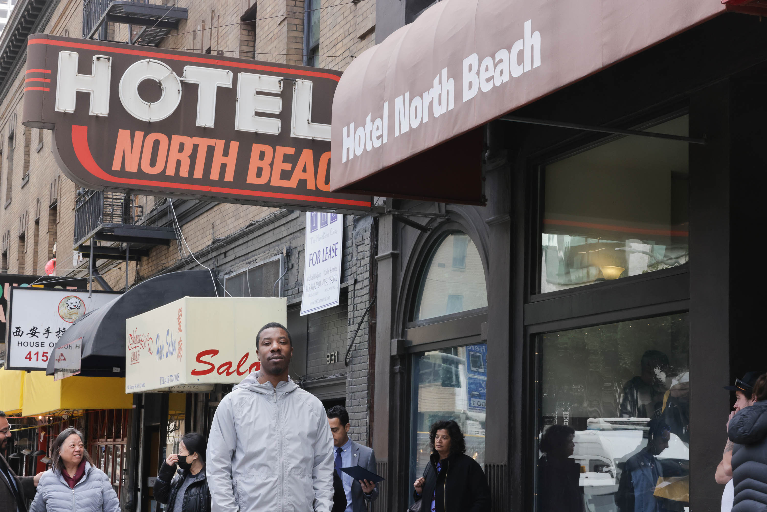 a man walks past an awning and a sign reading Hotel North Beach
