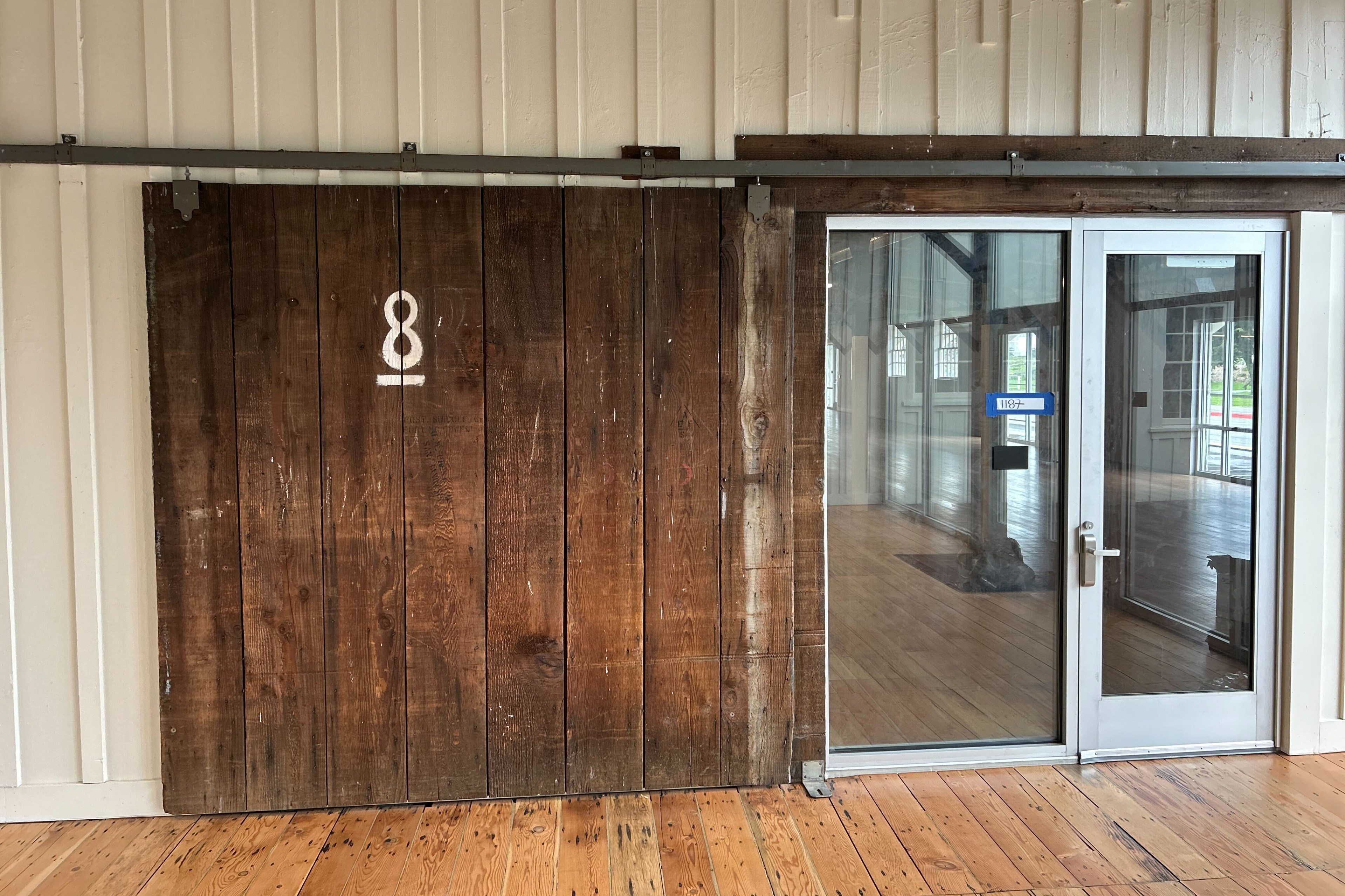 A rustic wooden sliding barn door next to modern glass doors inside a room with wooden floors.