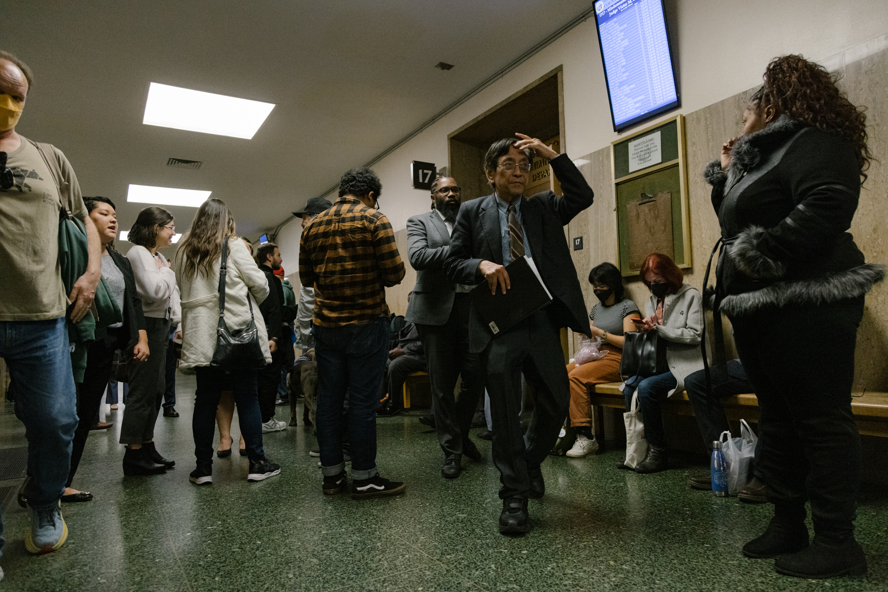 People fill the hall outside of a courtroom. 
