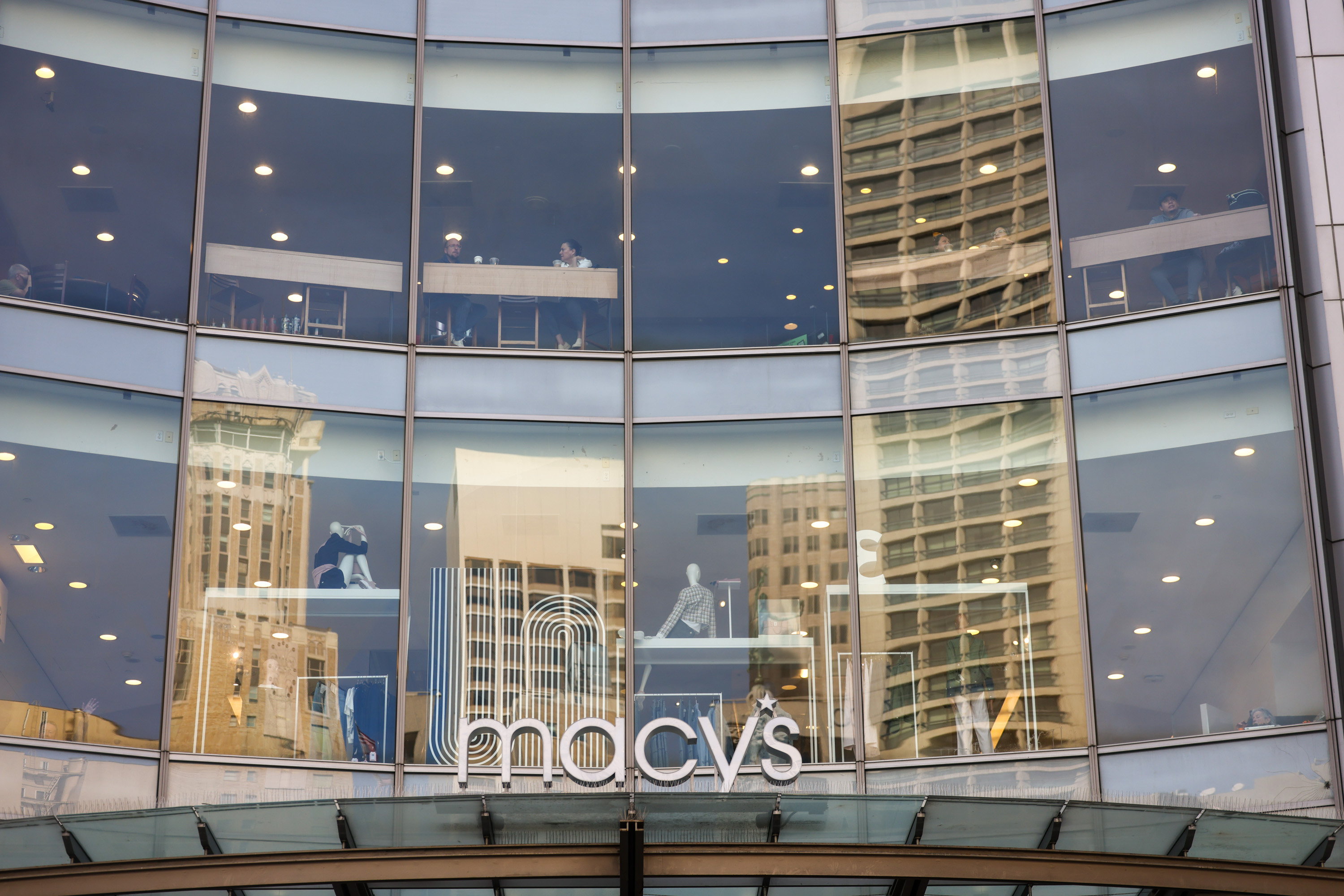The image shows Macy's store windows reflecting buildings, with people visible inside.