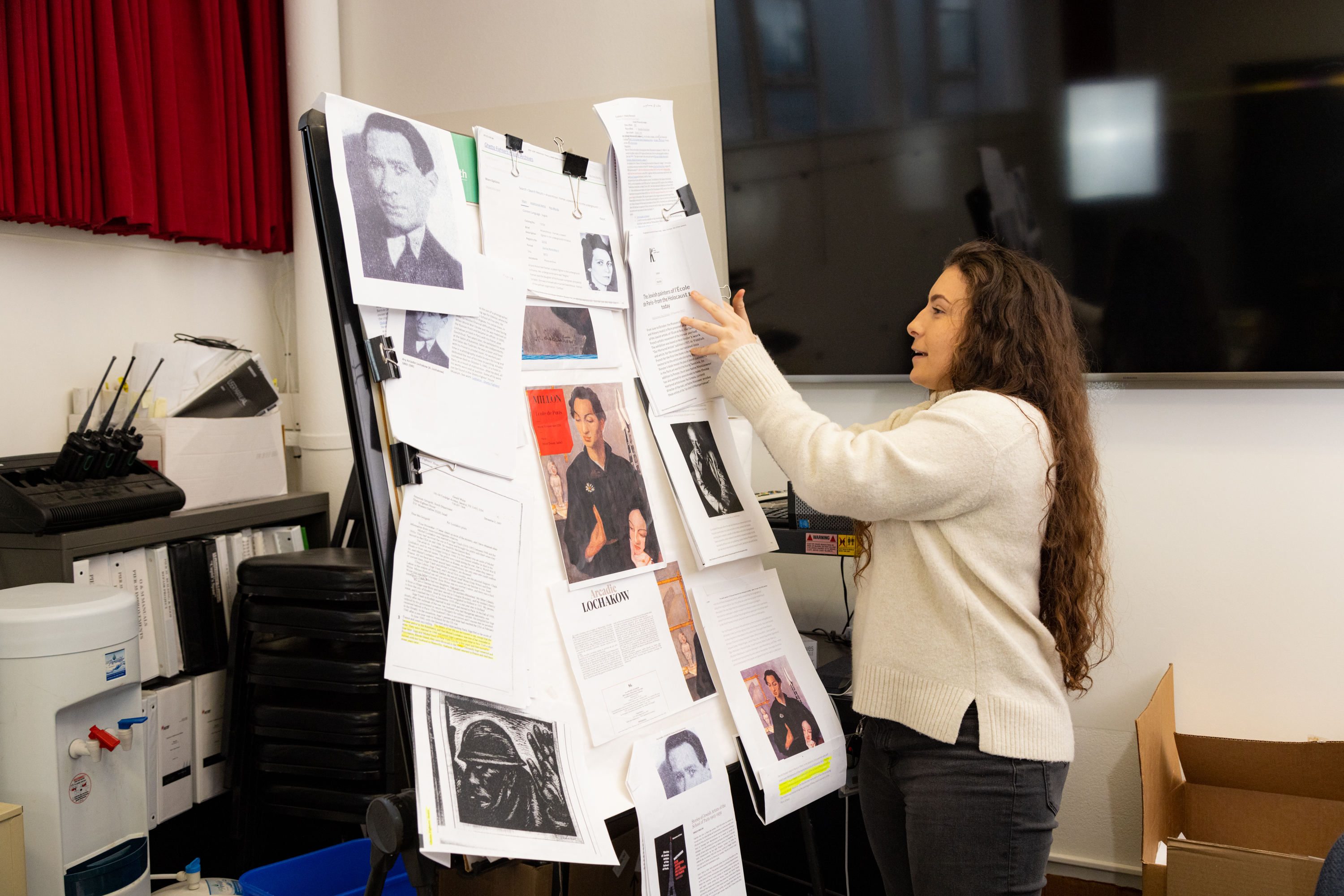 A woman in an office is arranging papers with text and images on a presentation board.