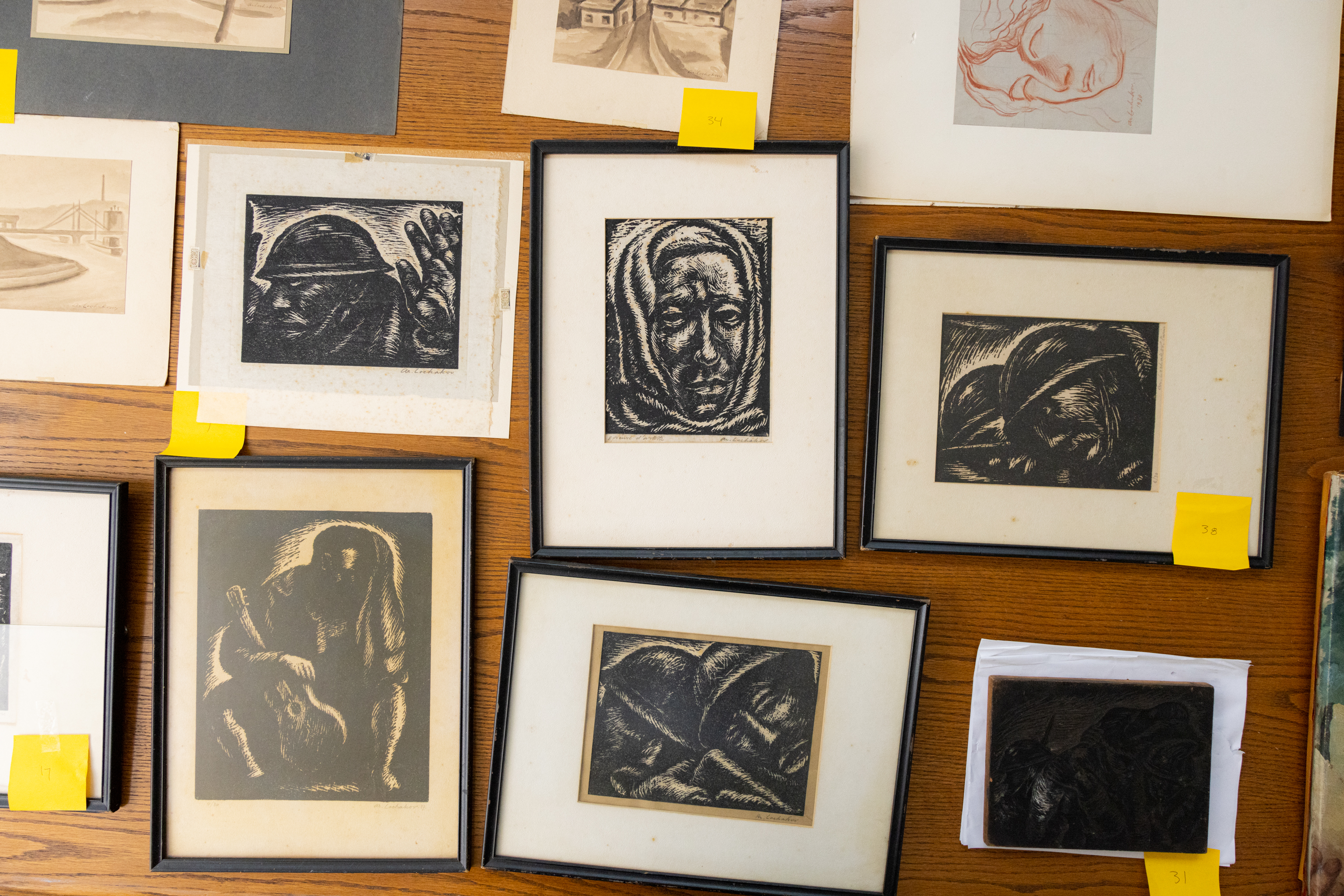 Collection of framed monochrome artworks displayed on wood, depicting various figures and abstract forms, with numbered labels.