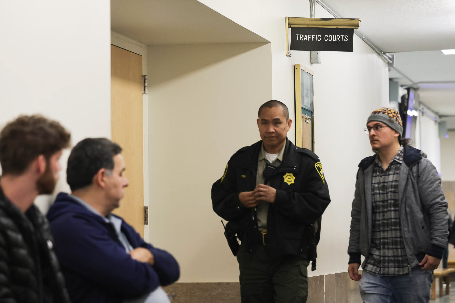 Three people look at a Sheriff's Department deputy standing outside a doorway.
