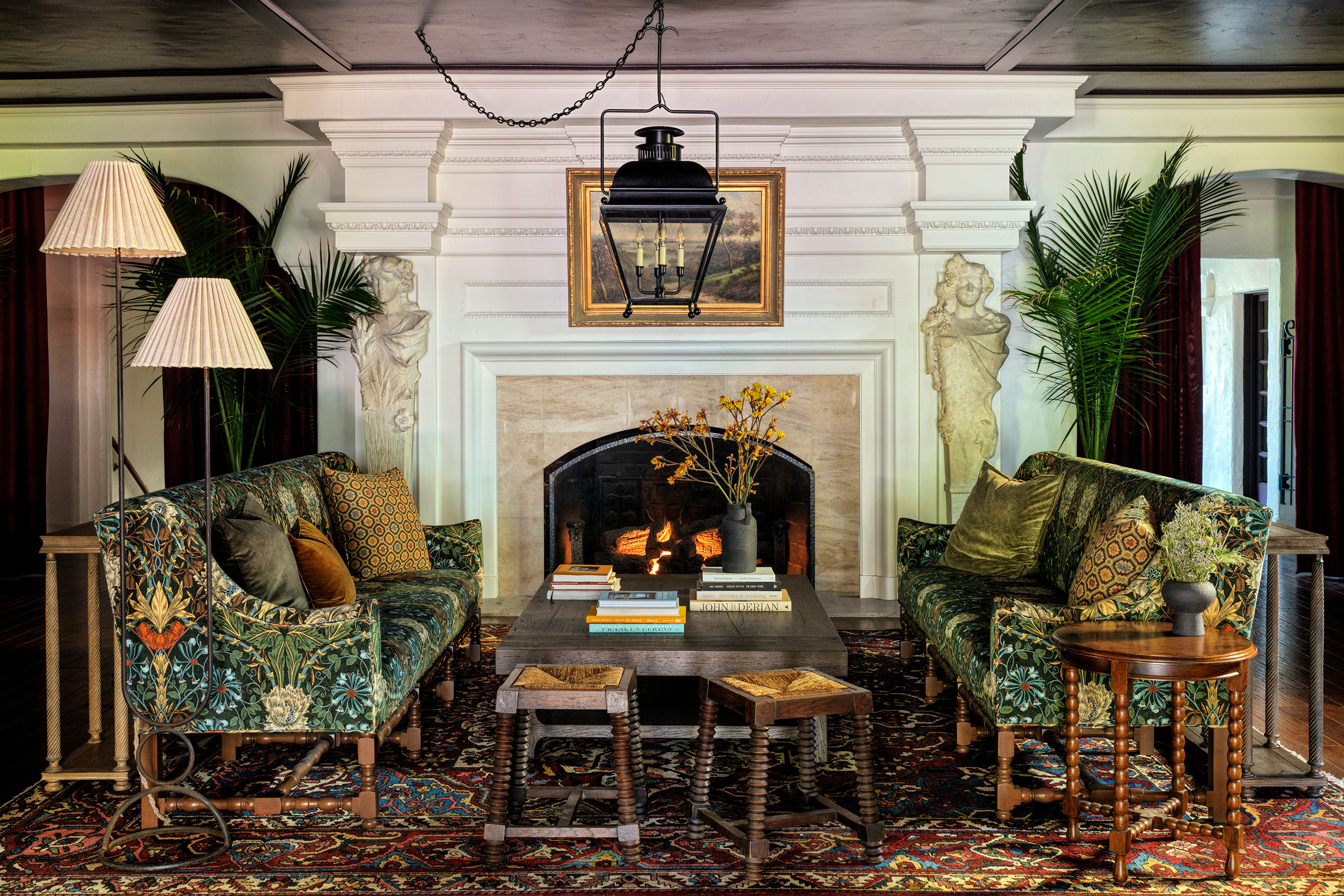 Two couches with a green and floral design sit across from a wooden coffee table in front of an ornate fireplace