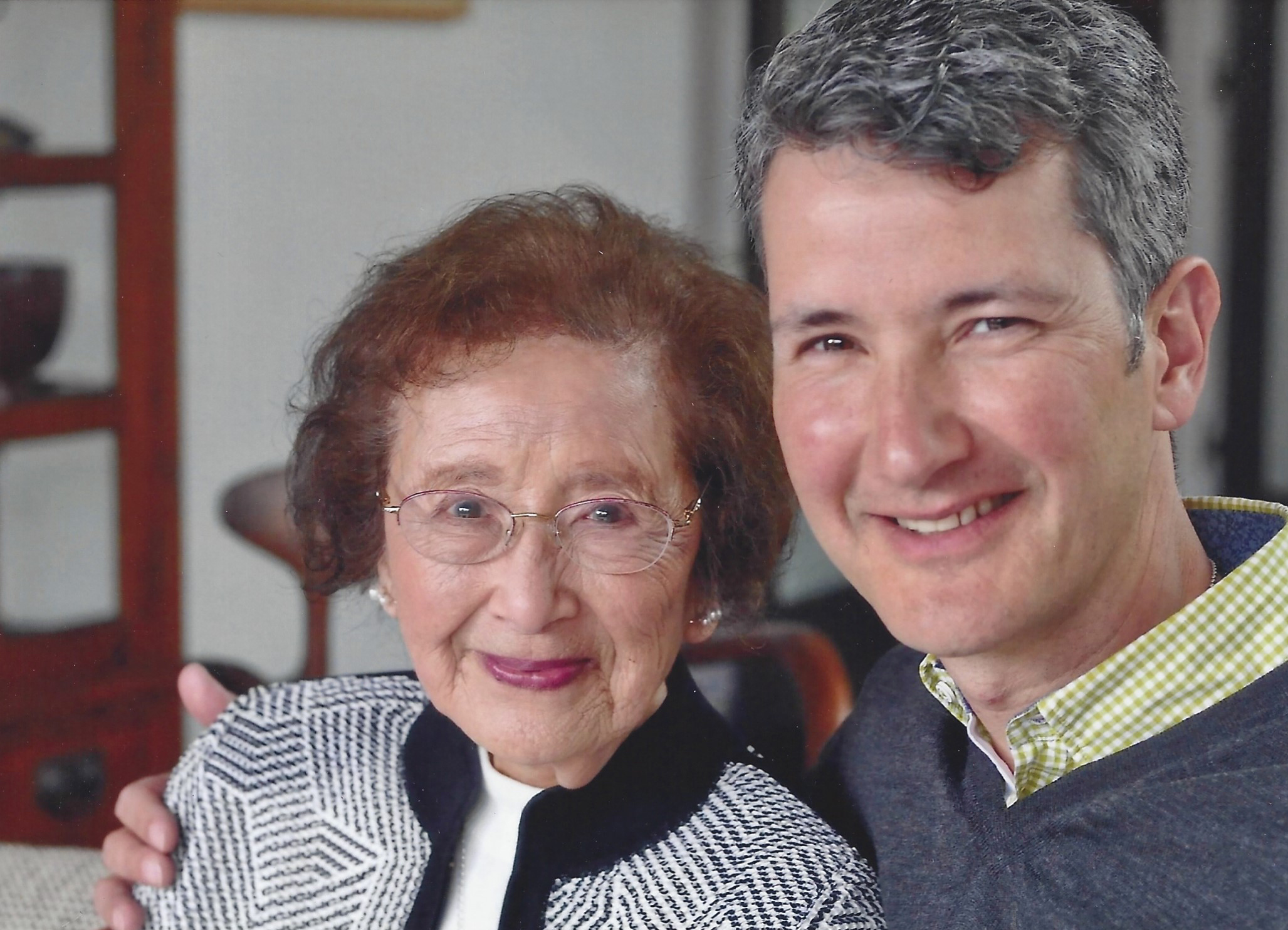 An elderly woman with glasses and a younger man smiling close together, likely family.