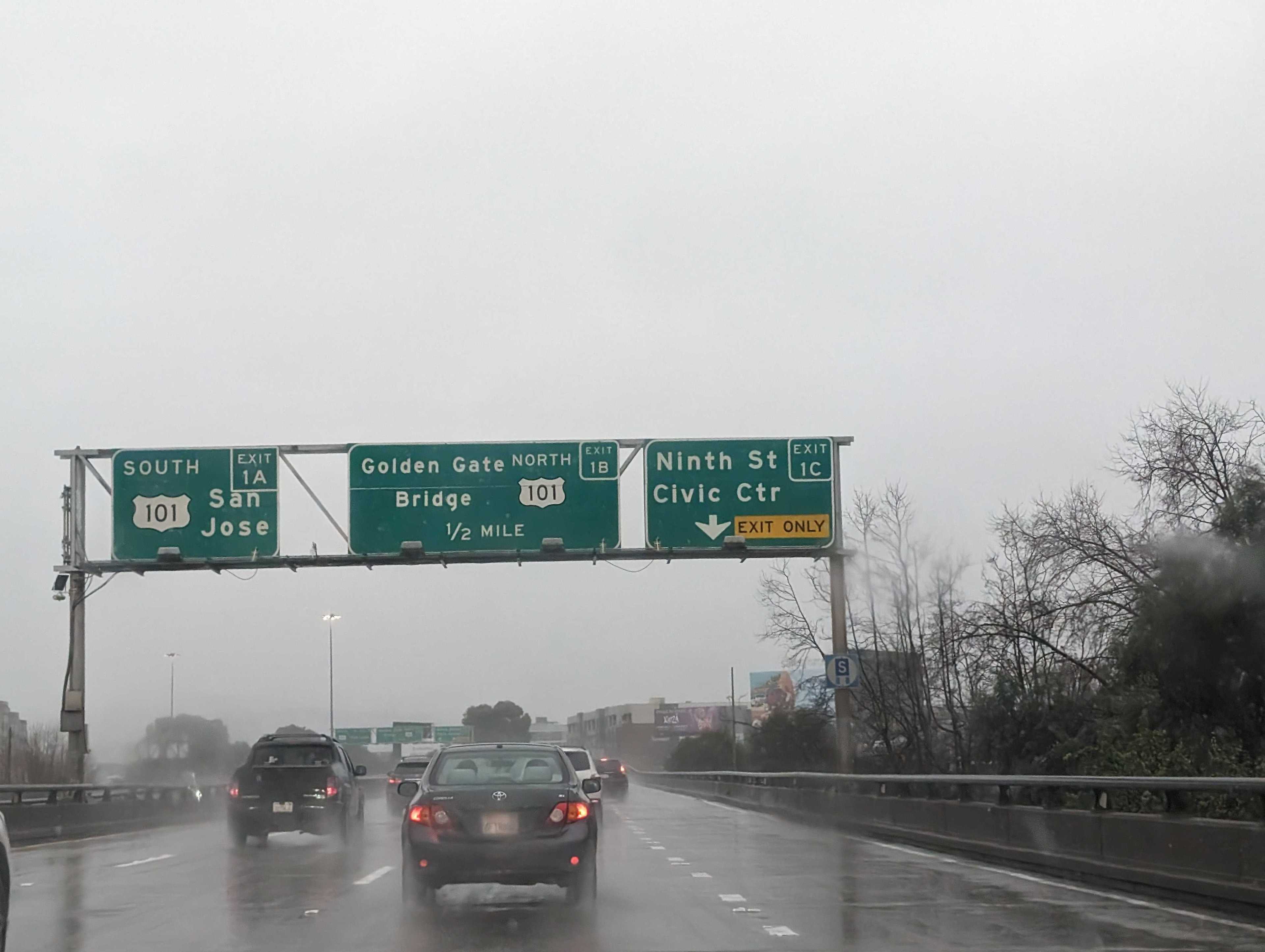 Cars and trucks ride along a rain-soaked highway under road signs.