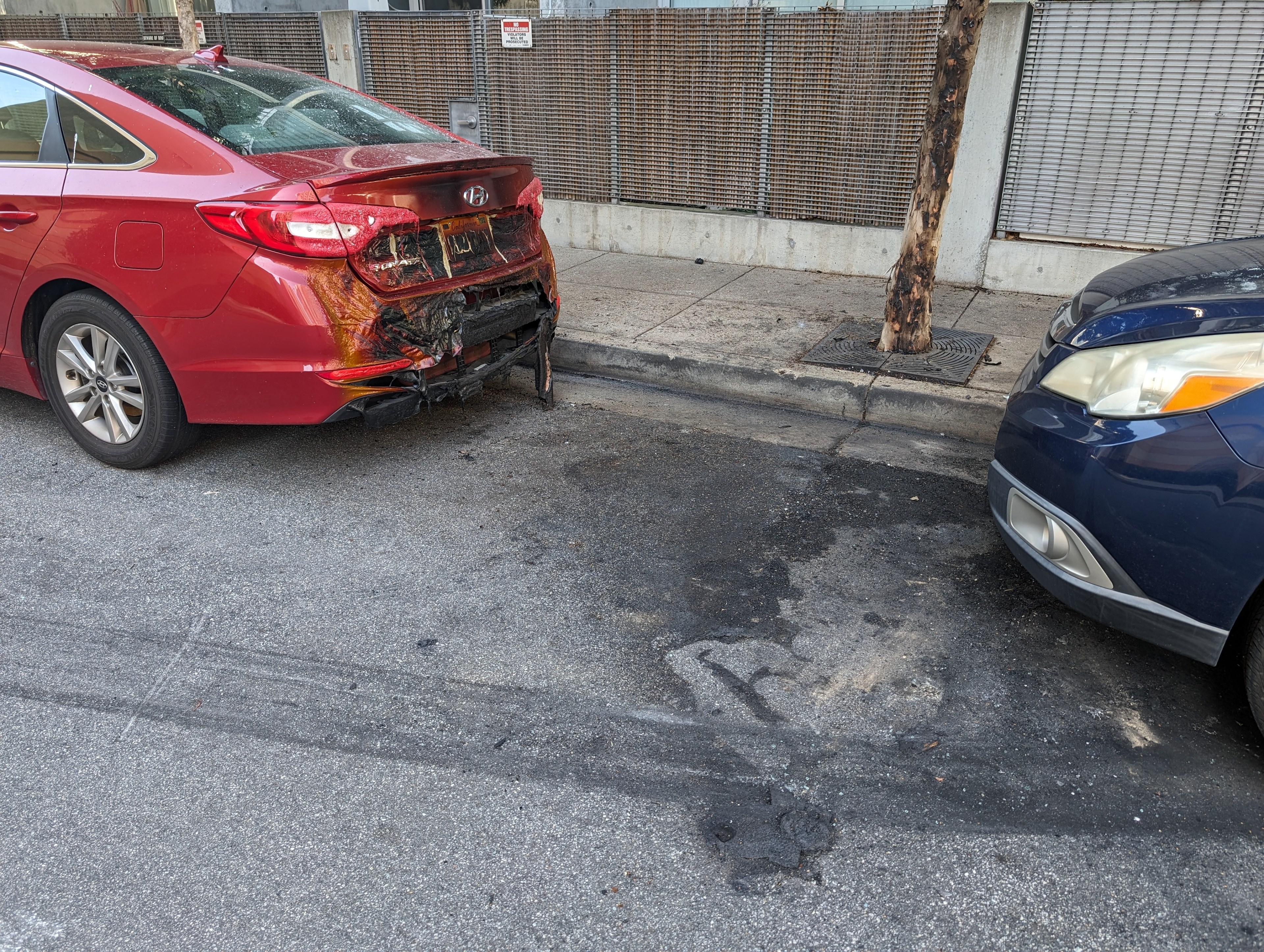 A parked vehicle's rear bumper is blackened by a vehicle fire a day earlier