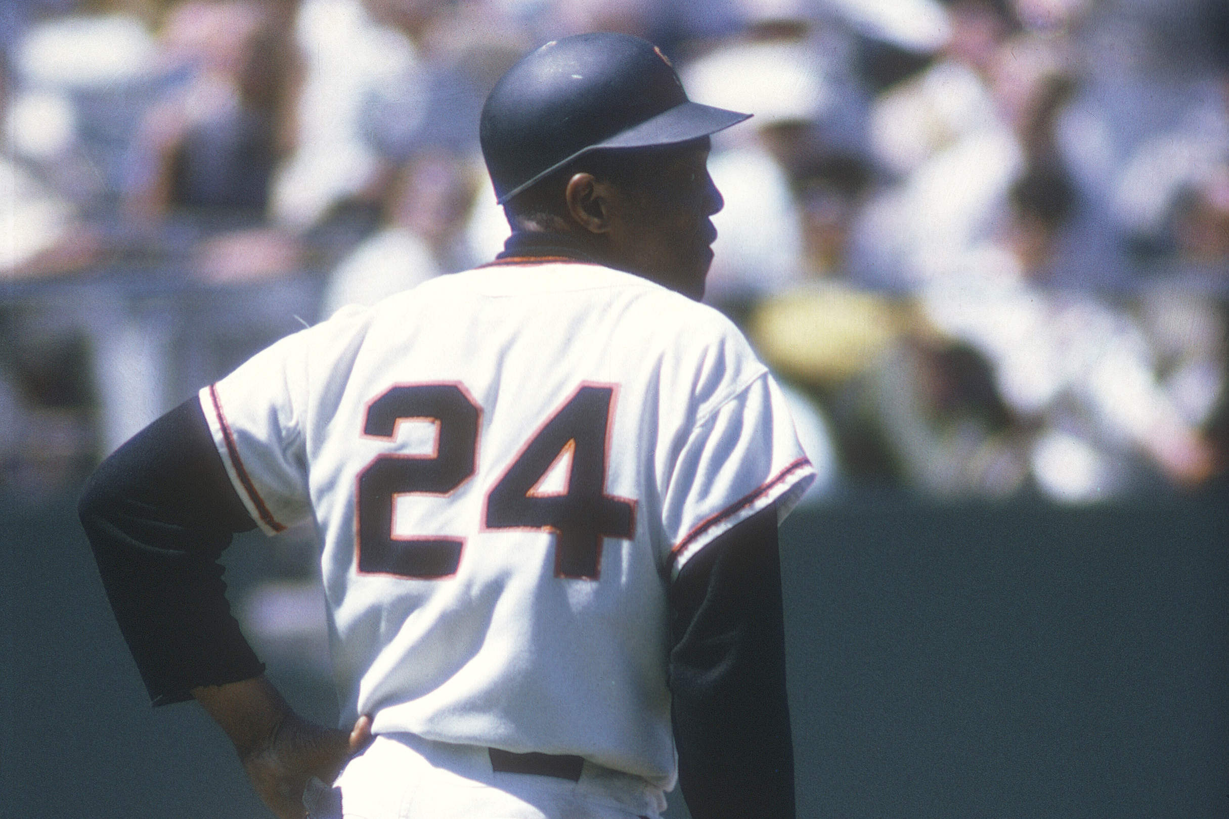 A baseball player in a white and red uniform with the number 24 is standing on a field, viewed from the back.
