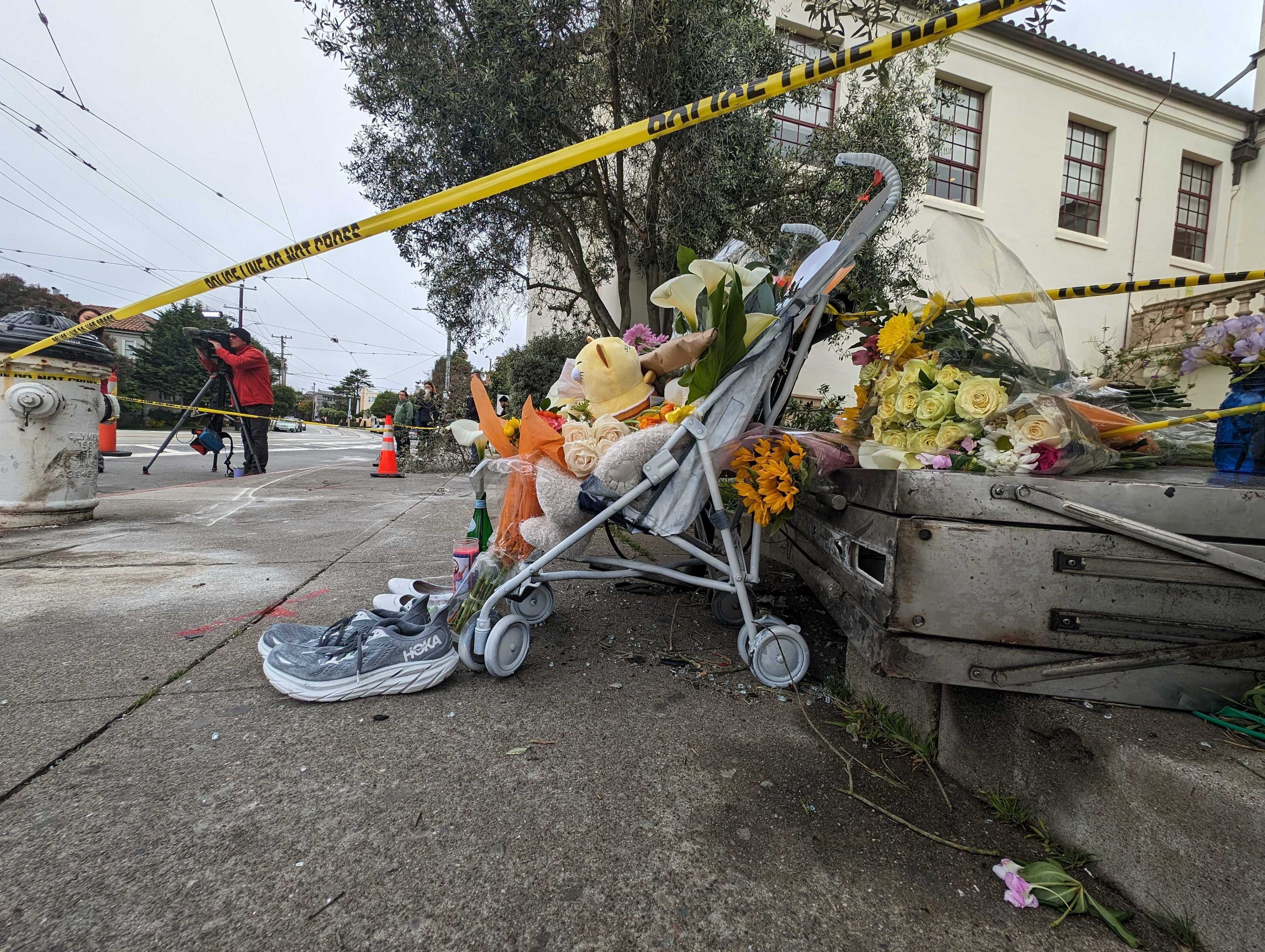 A street corner with flowers, a stroller, and a caution tape, suggesting a makeshift memorial.