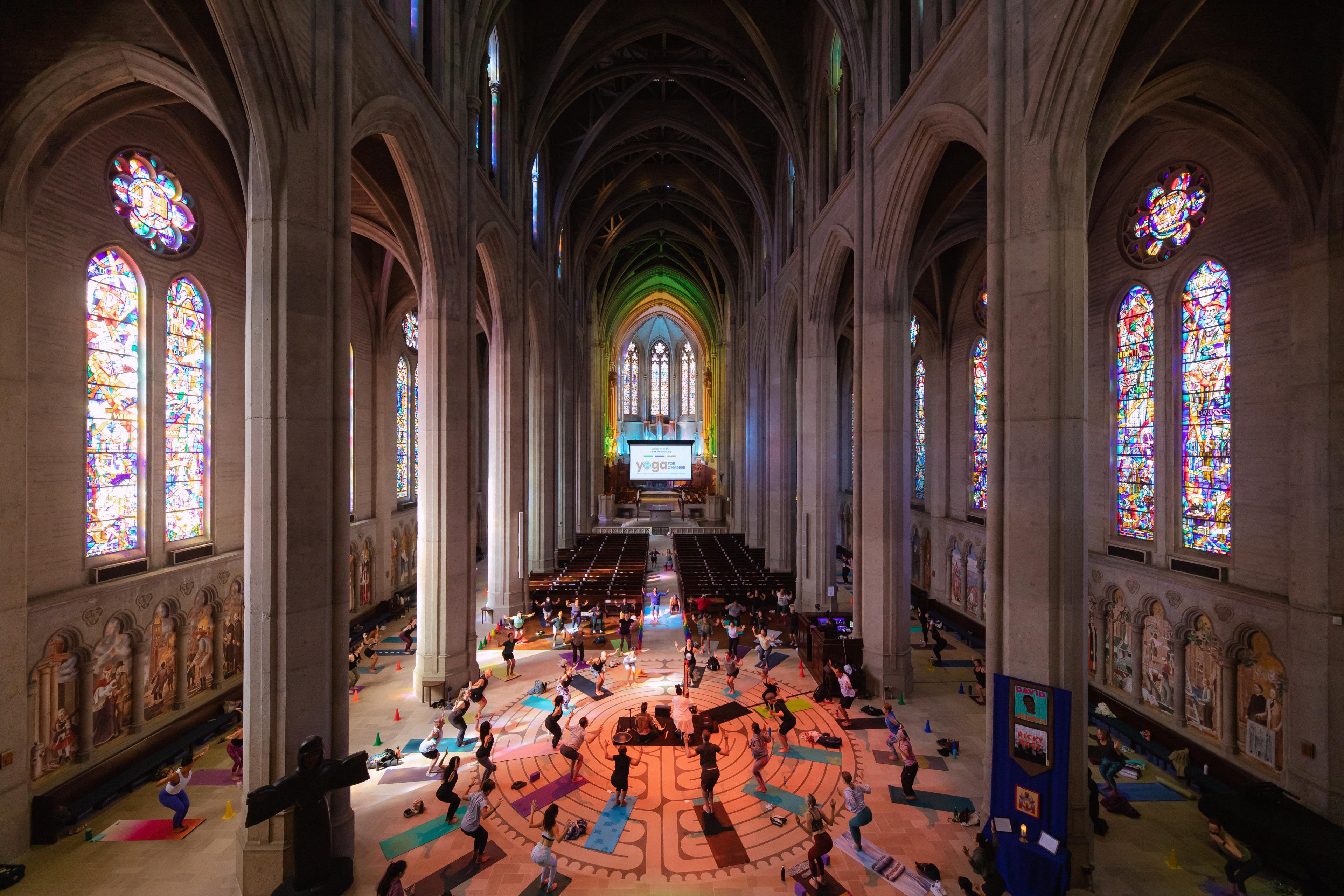 A yoga class inside a cathedral with high ceilings and vibrant stained glass windows.
