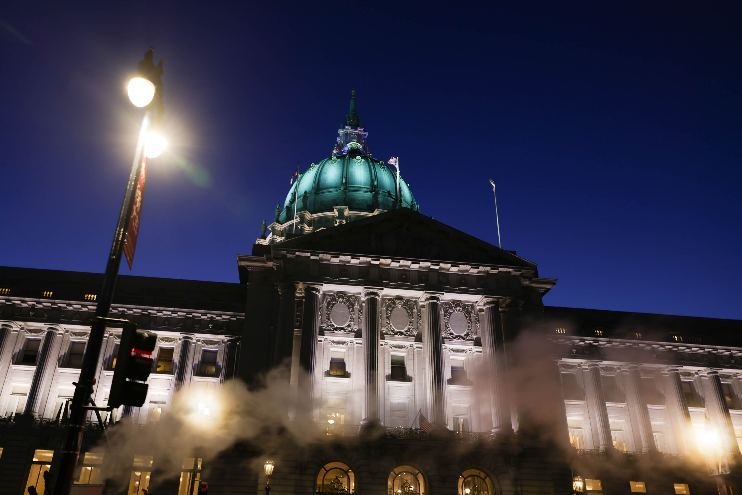 A neoclassical building at dusk with a lit dome and streetlight, obscured partially by steam.