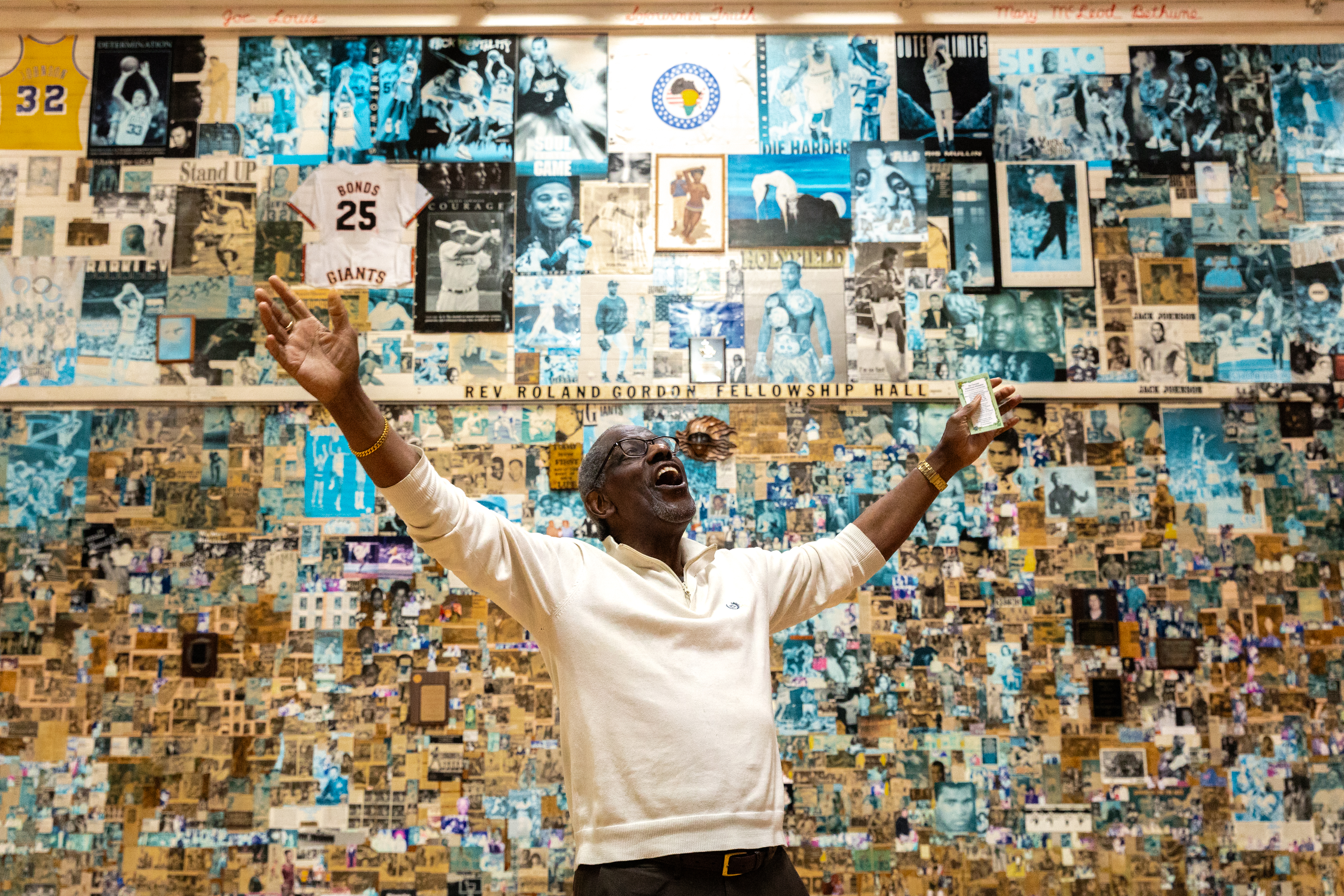 A joyful man raises his arms in a room covered with numerous historical photos and memorabilia.