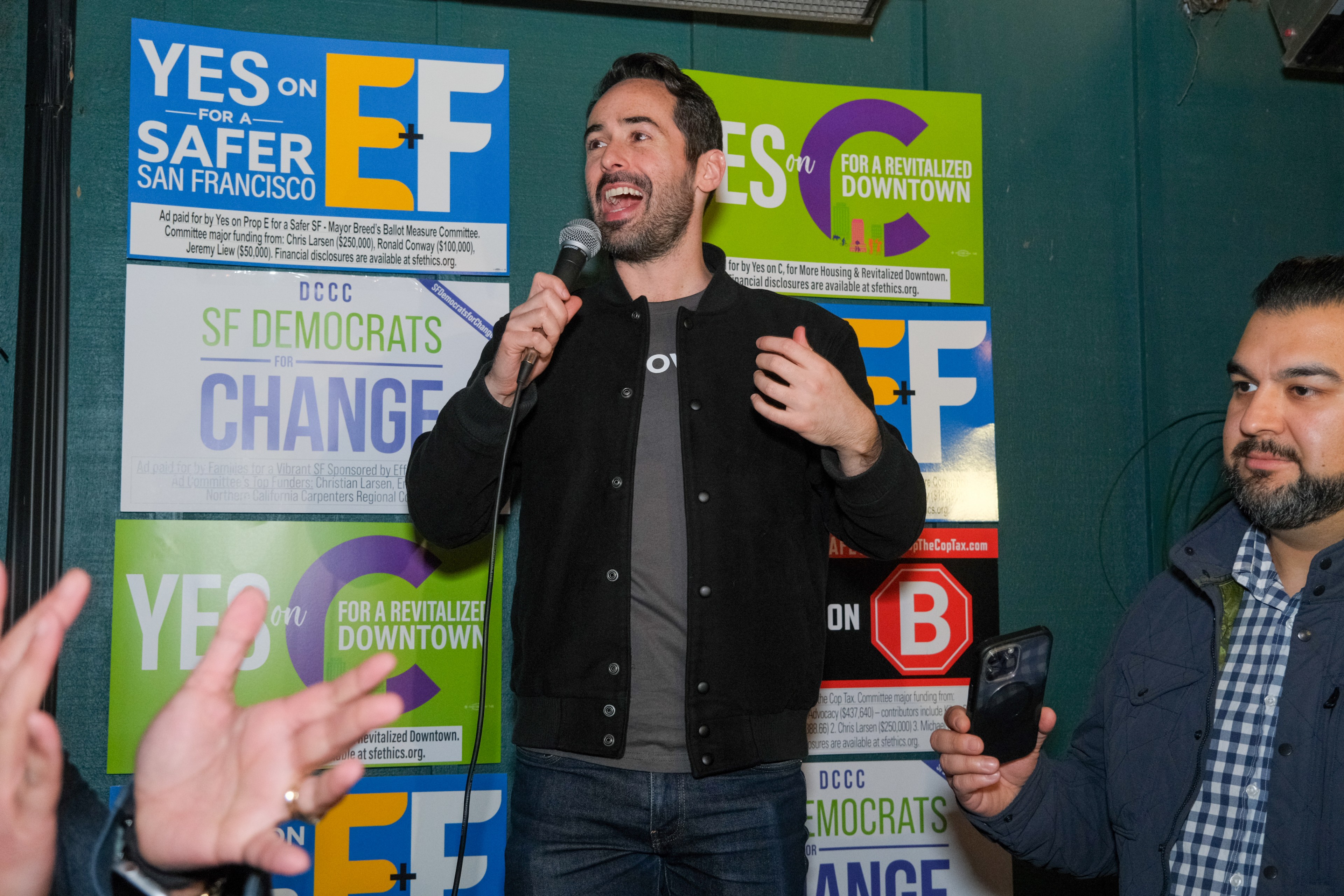 A man holding a microphone speaks in front of picket signs. 