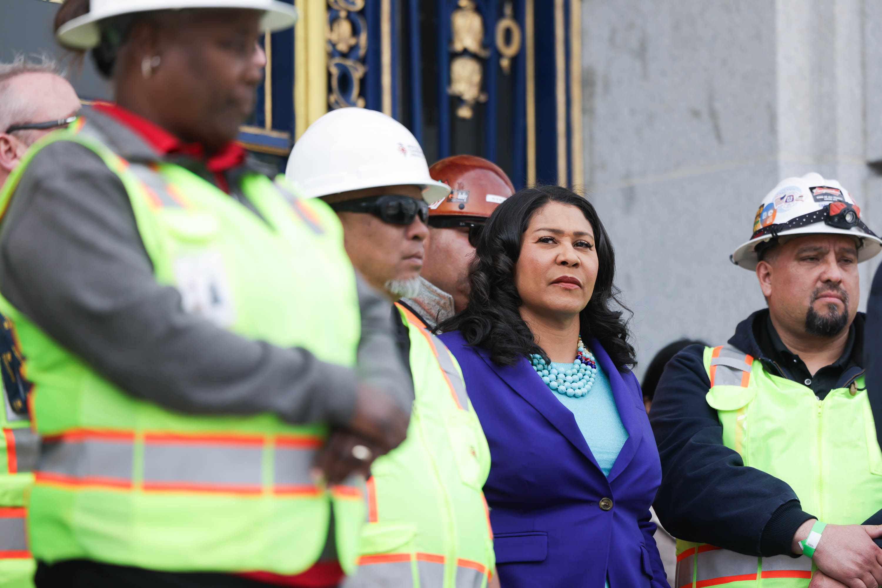 A group of people in safety vests and hard hats, with a woman in a purple blazer standing out at the center.