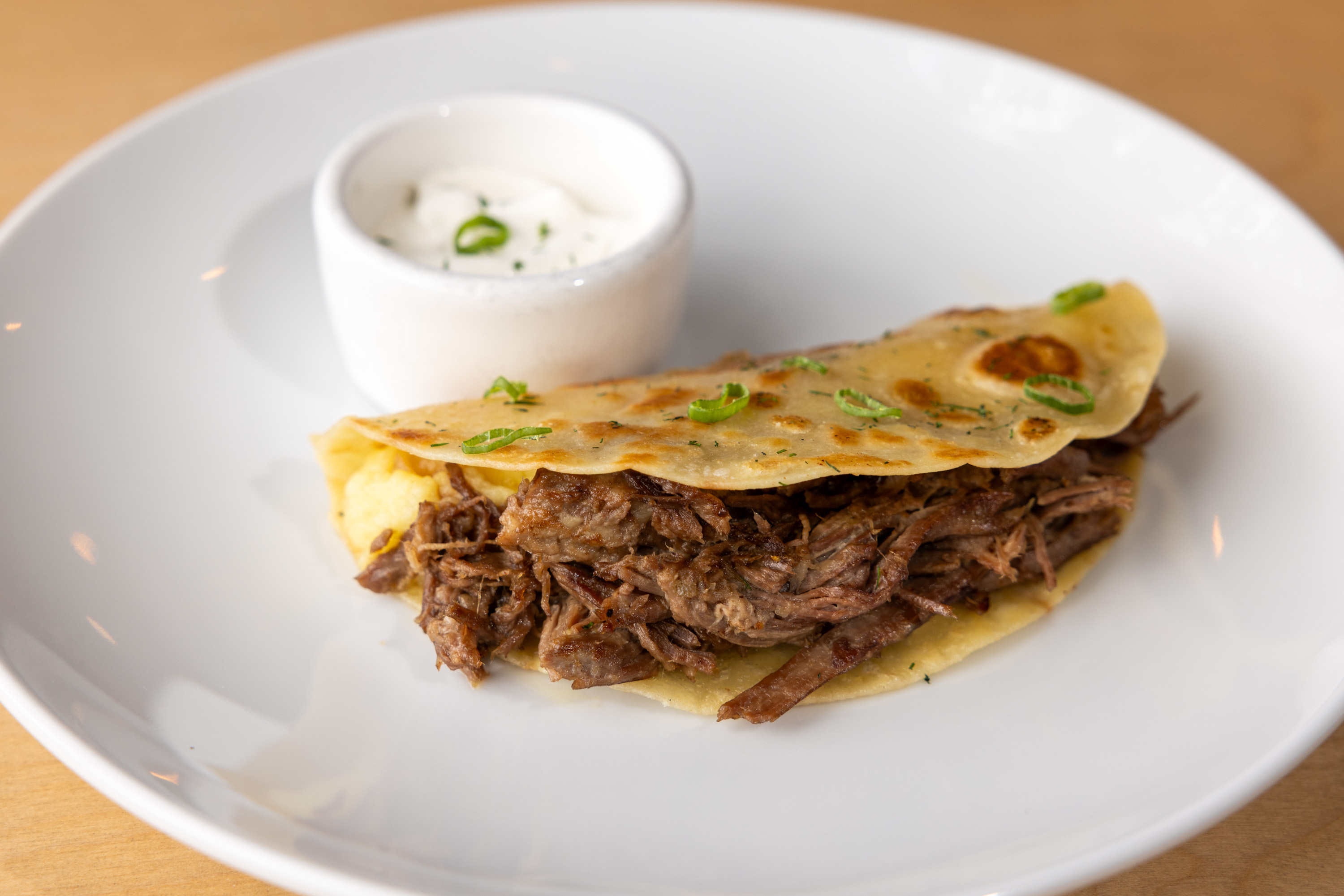 A quesadilla with shredded meat and cheese on a plate with a cup of sauce.